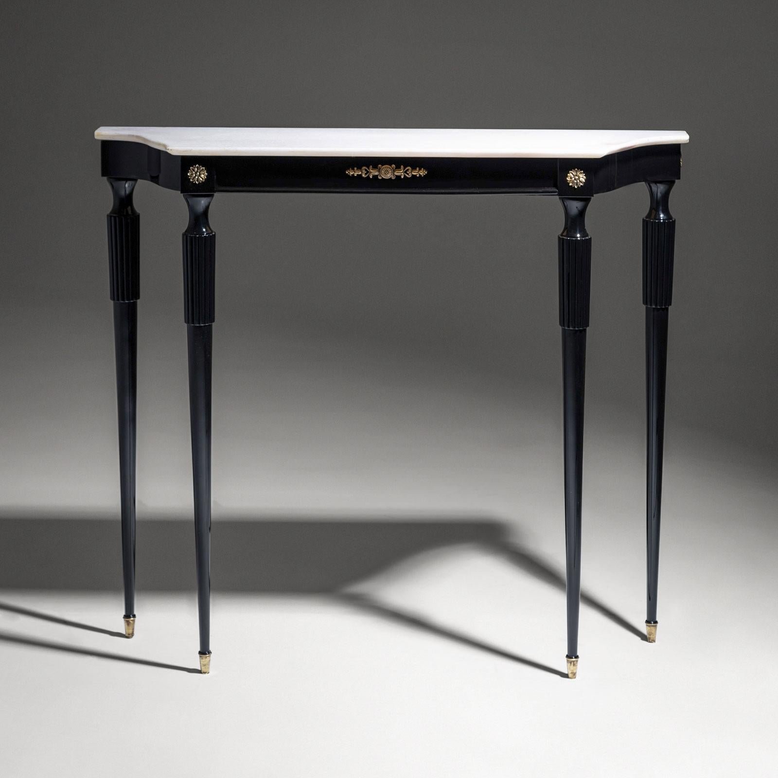 An elegant and delicate console table from Italy, crafted in the mid-20th century. The table stands on tall, tapered legs with brass sabots and features decorative brass appliqués on the apron.

The trapezoidal shape adds a modern sense of
