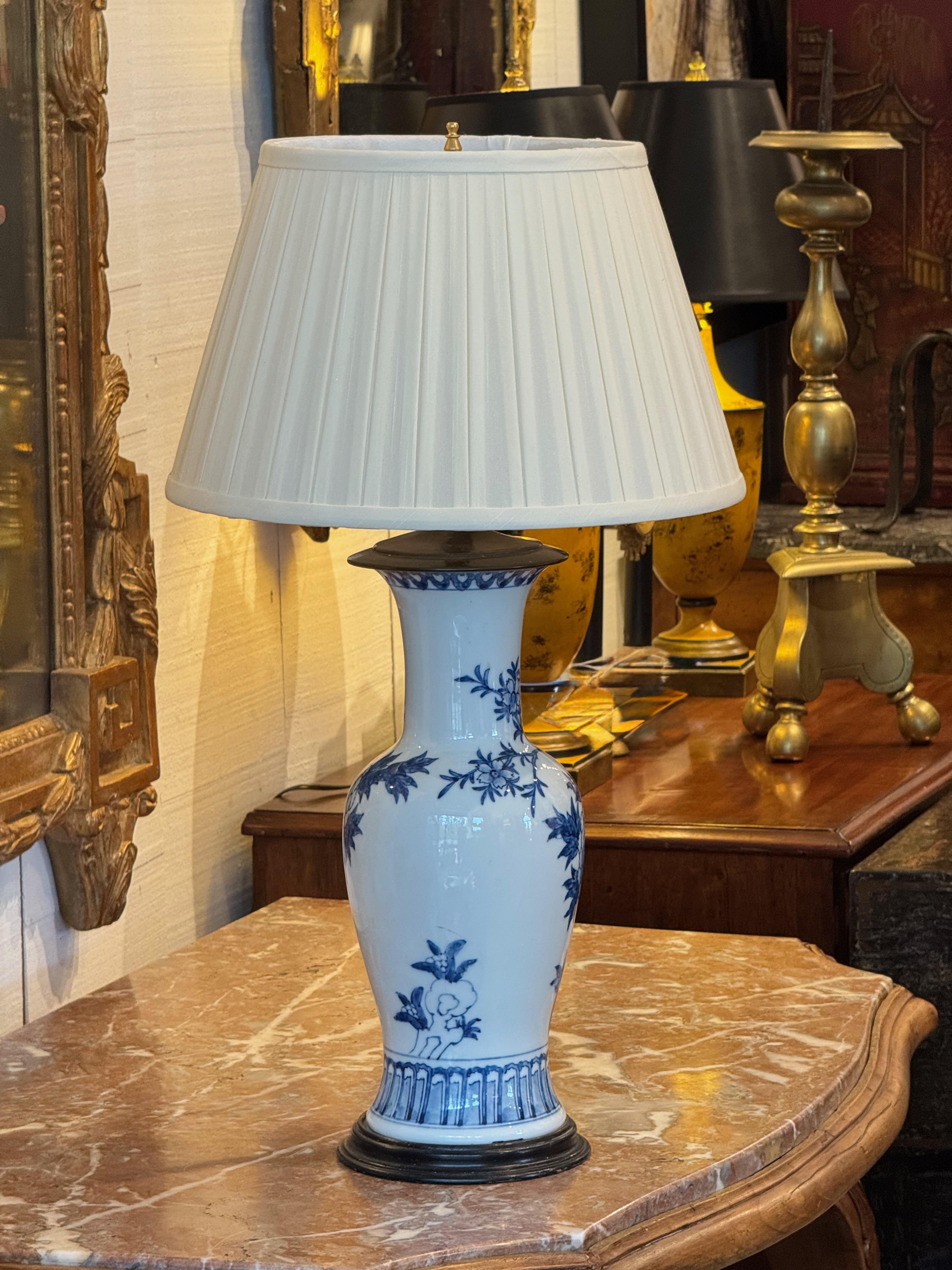 Blue and white porcelain lamp in the style of traditional Chinese export ware, converted from a vase form. The body features hand-painted floral and foliate decoration with a ribbed border at the base. Mounted on a dark wood base and paired with a