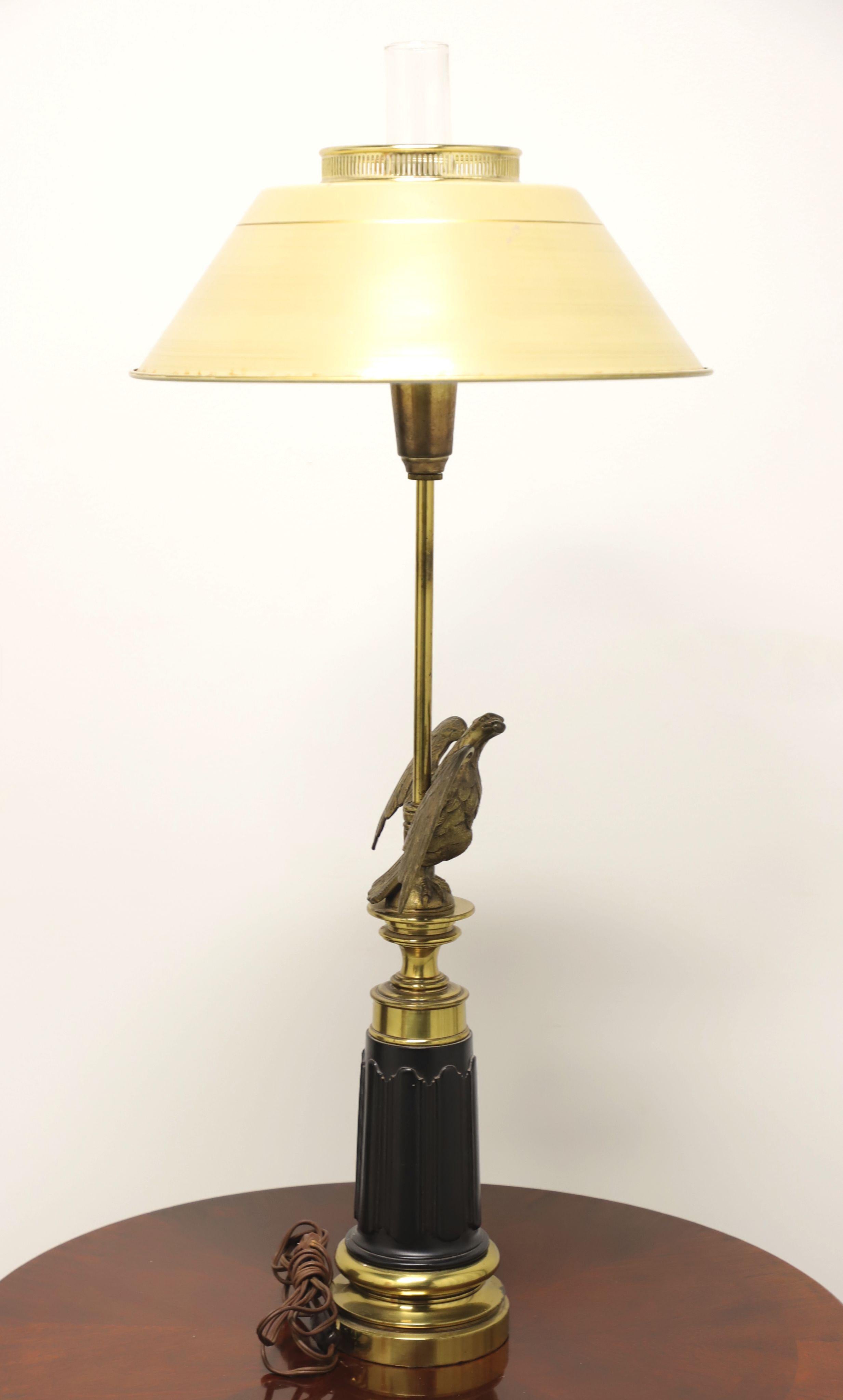 An Americana style American Eagle table lamp, unbranded. Solid brass with eagle perched on base, dark metal in center of base adds contrast and candlestick shaft to light fixture. Glass chimney inserts into light fixture and metal shade rests on