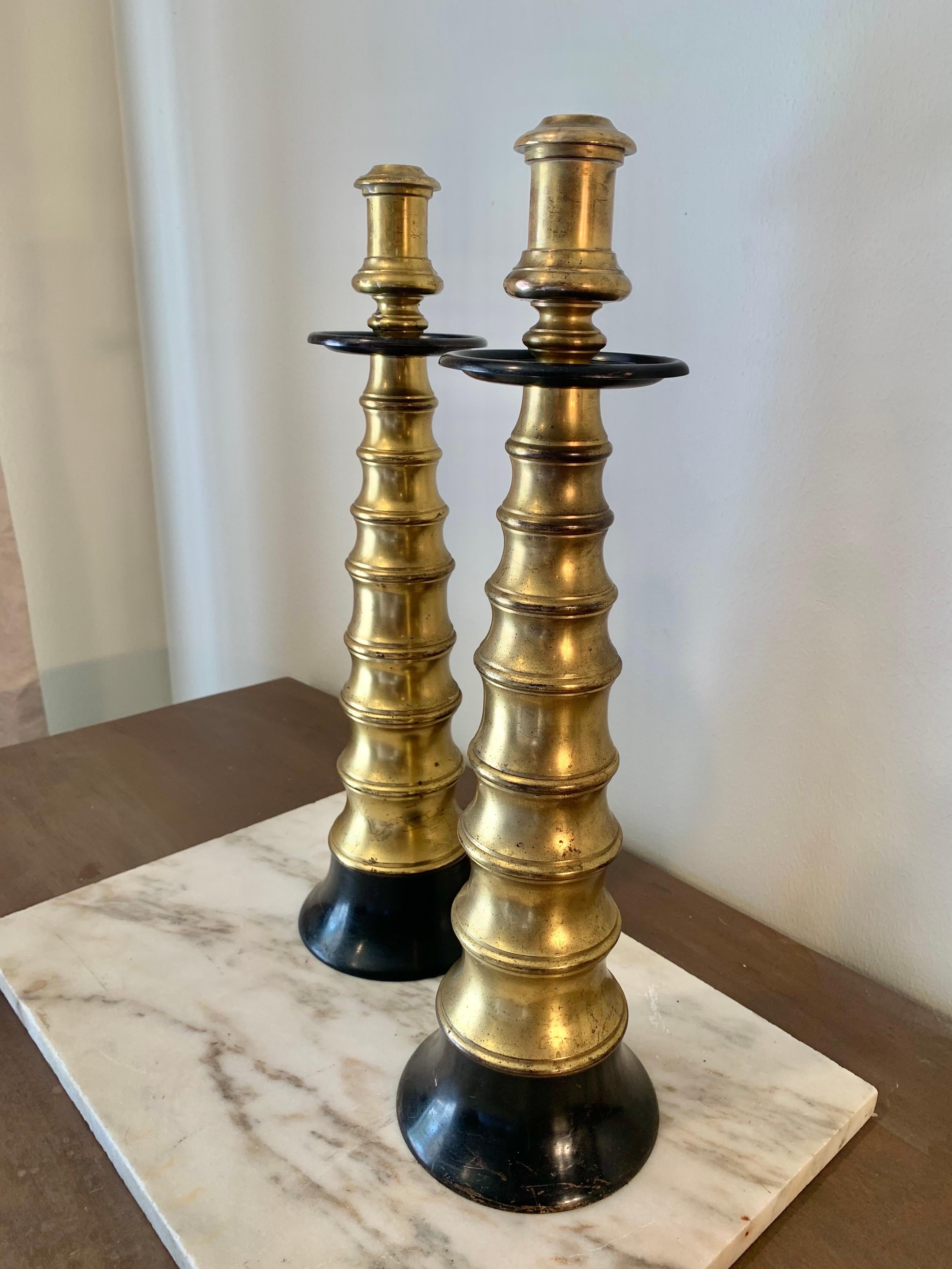 This pair of impressive Mid 20th Century Candleholders are crafted from brass in a detailed turned fashion. The wax drip catcher and round base are both ebonized to add eye catching detail to both pieces. Each candlestick is fitted to hold a