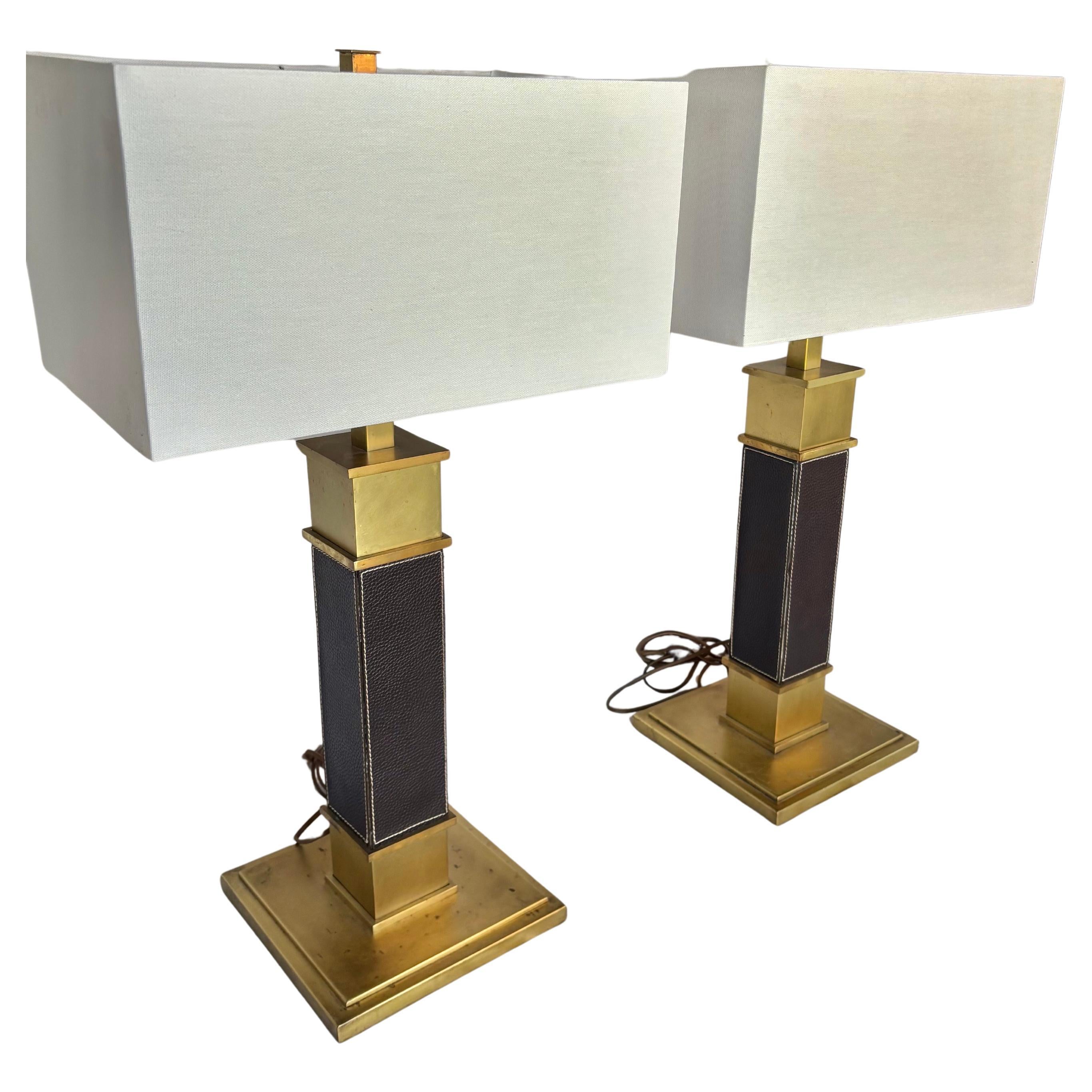 Cette paire de lampes de table du milieu du XXe siècle a été fabriquée en laiton lourd et en cuir au milieu des années 1900. Les lampes présentent un abat-jour rectangulaire menant à un corps en laiton qui a été recouvert de cuir noir avec des