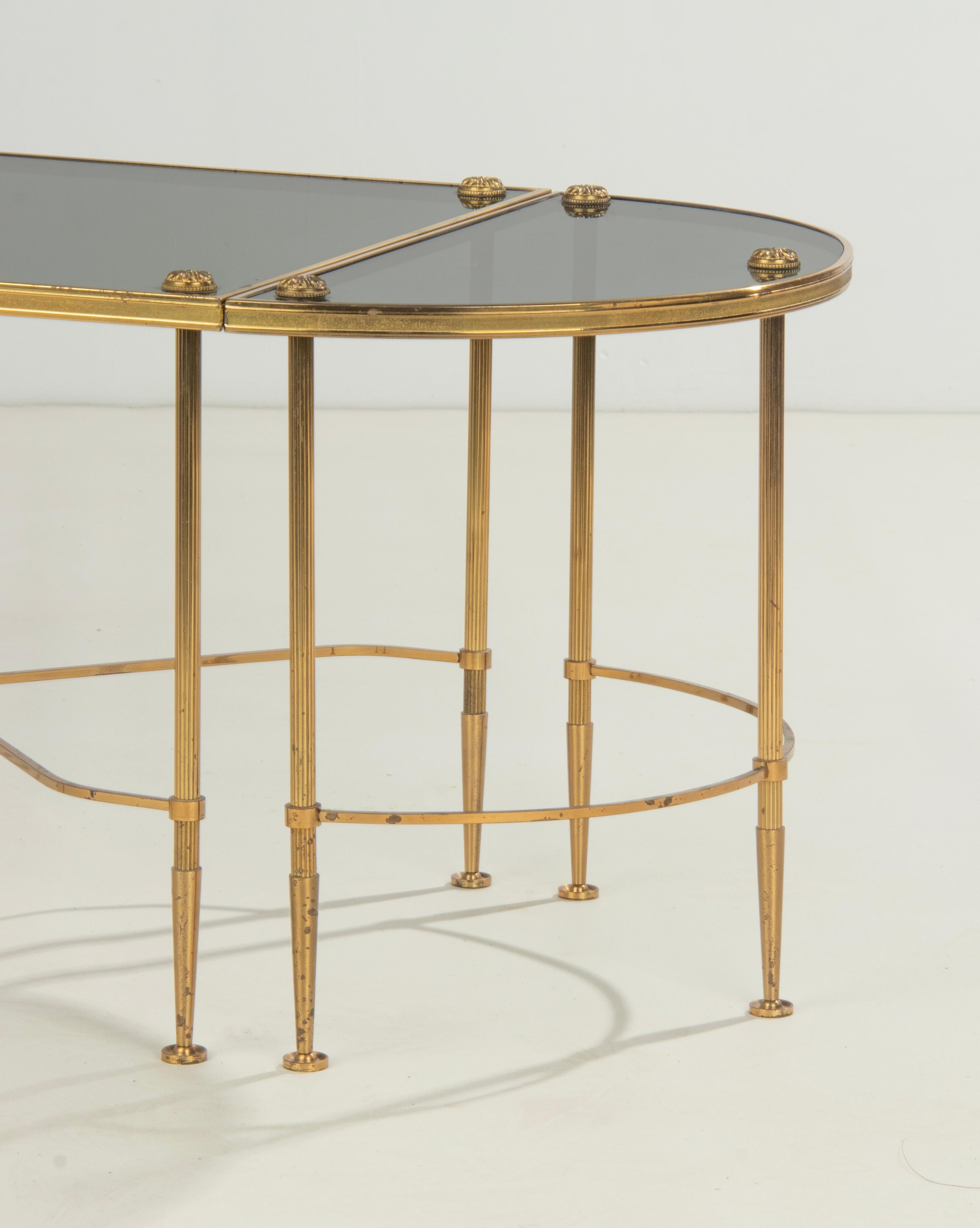 An elegant Maison Baguès style coffee table, made of polished brass colored metal, on fluted legs. Three modular elements: a central rectangular table with a x-stretcher, accompanied by two half-moons (demi lune) on both ends. On top a smoked
