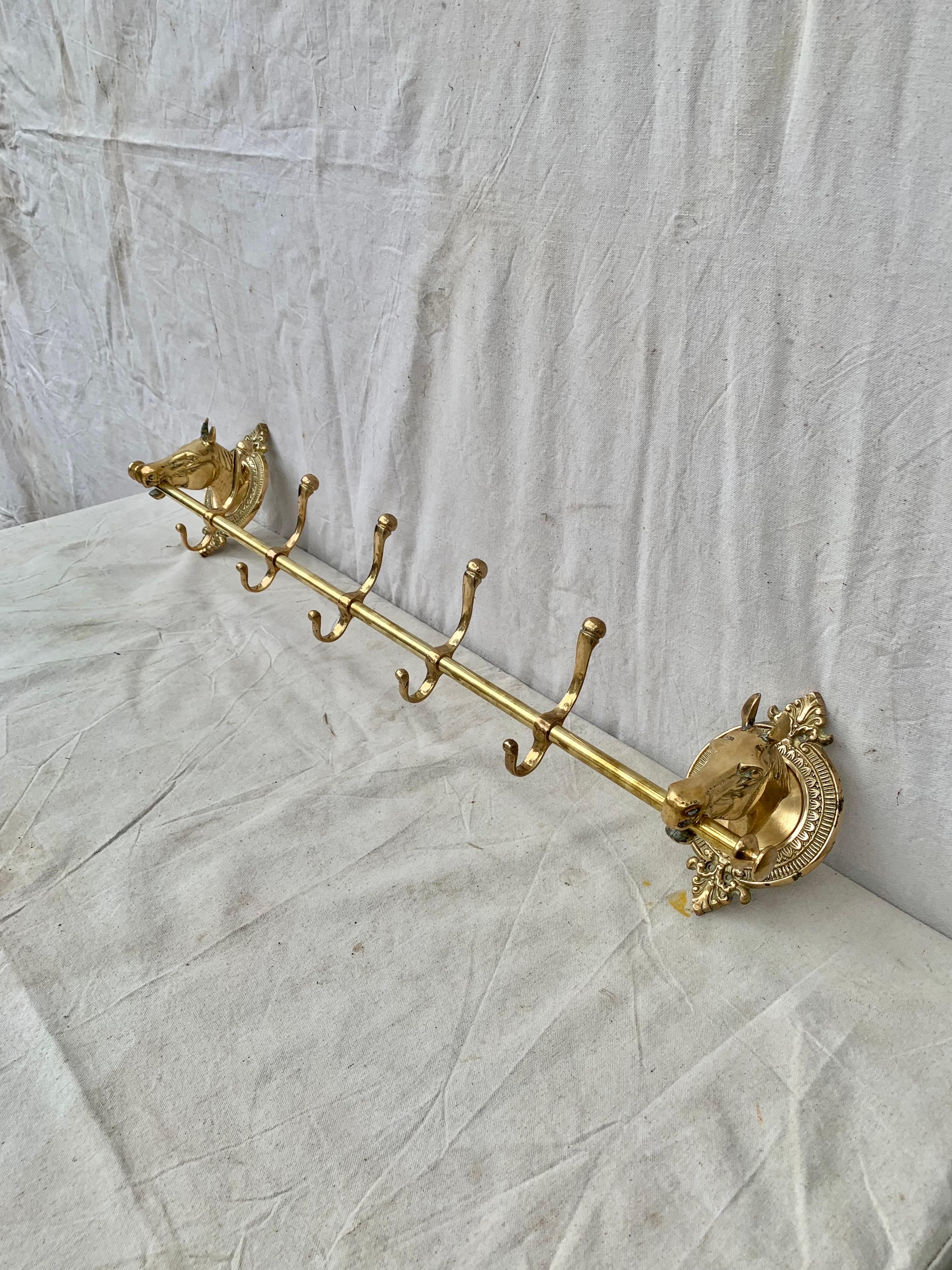 This large Mid 20th Century Horse Head Coat Rack was crafted from brass in the mid 1900's. The piece features two horse heads mounted on intricately detailed oval brass plaques that are adjoined by a center rod containing five hooks. Both the horse