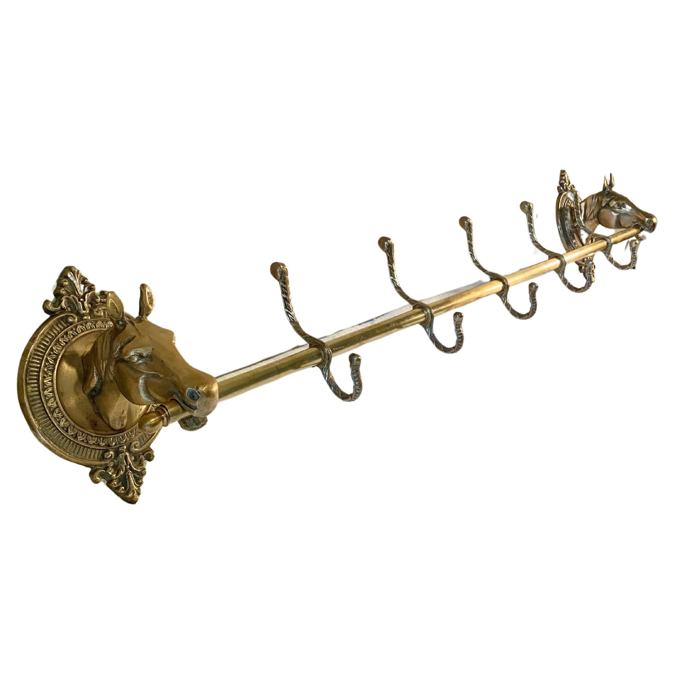 This large Mid 20th Century Horse Head Coat or Hat Rack was crafted from brass in the mid 1900's. The piece features two horse heads mounted on intricately detailed oval brass plaques that are adjoined by a center rod containing five hooks. Both the