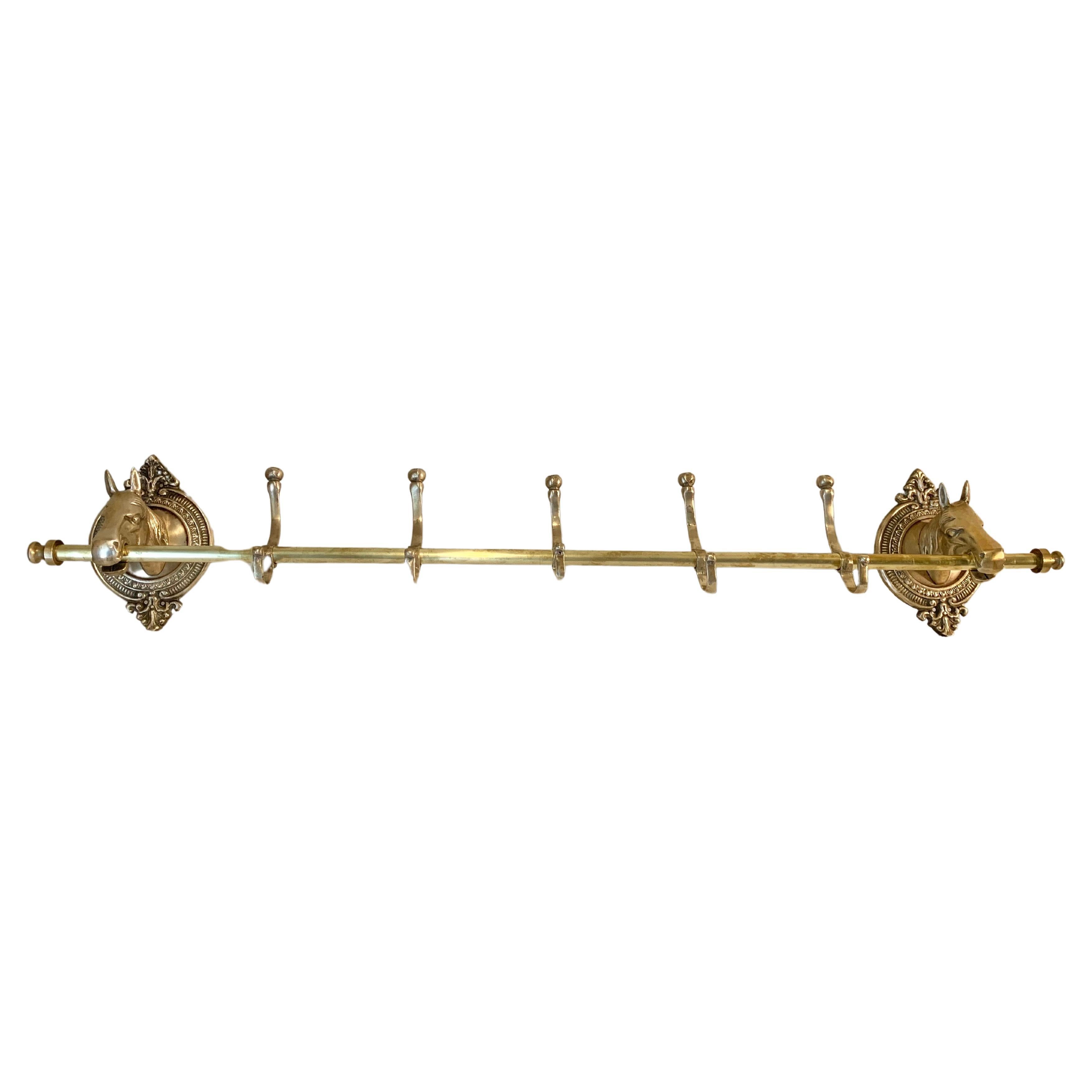 This large Mid 20th Century Horse Head Coat or Hat Rack was crafted from brass in the mid 1900's. The piece features two horse heads mounted on intricately detailed oval brass plaques that are adjoined by a center rod containing five hooks. Both the