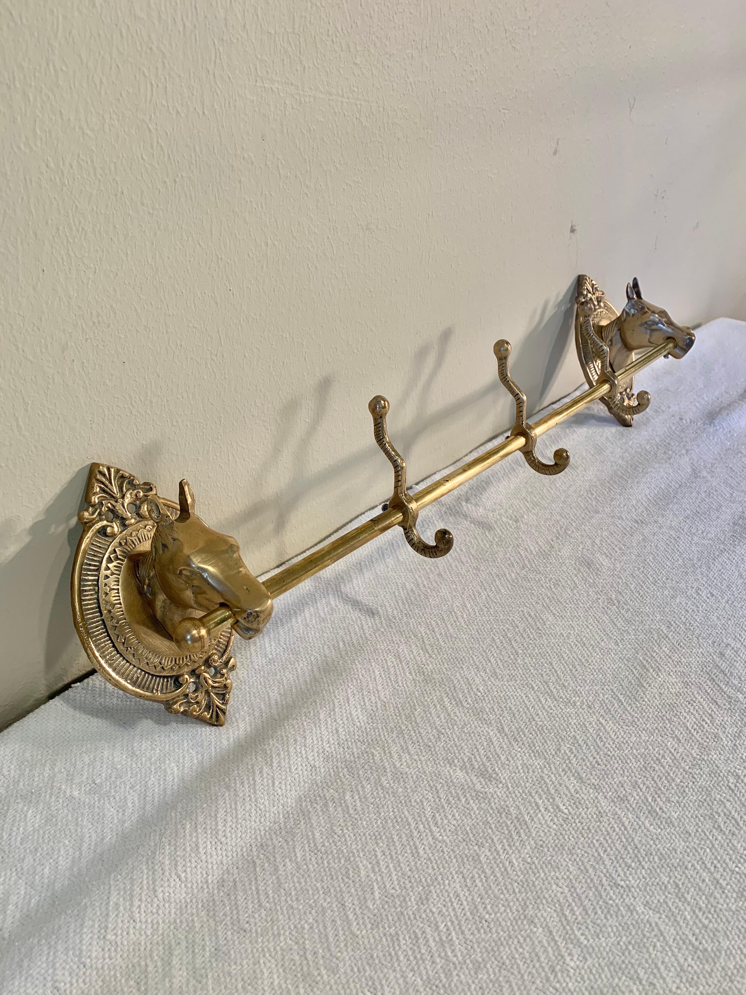 This Mid 20th Century Horse Head Coat or Hat Rack was crafted from brass in the mid 1900's. The piece features two horse heads mounted on intricately detailed oval brass plaques that are adjoined by a center rod containing three hooks. Both the
