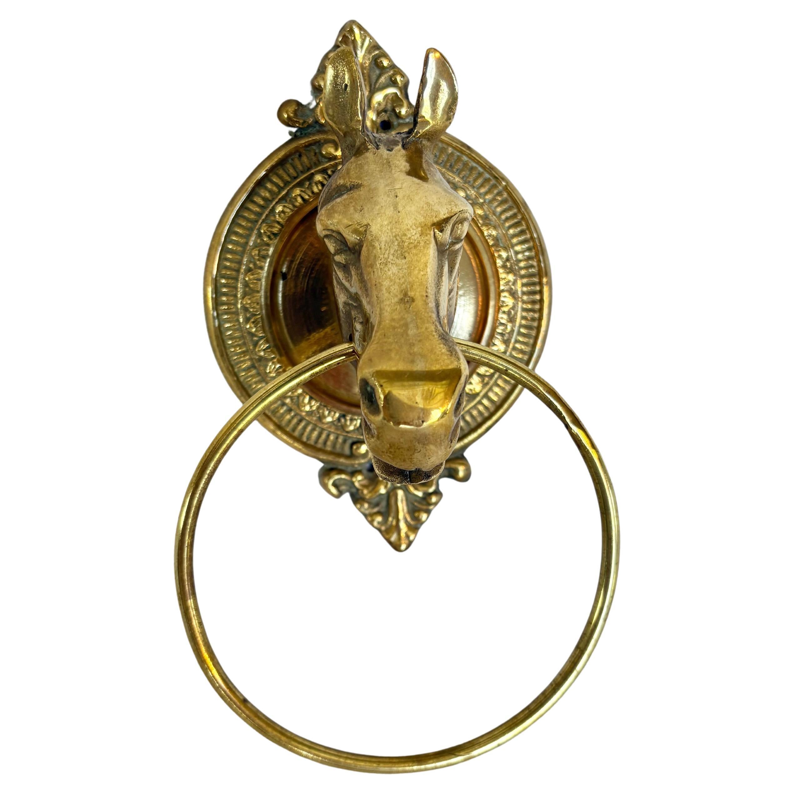 This Mid 20th Century Horse Head Towel Ring was crafted from brass in the mid 1900's. The piece features a horse head mounted on an intricately detailed oval brass plaque with a towel ring drop from behind the horses mouth. The brass shows great