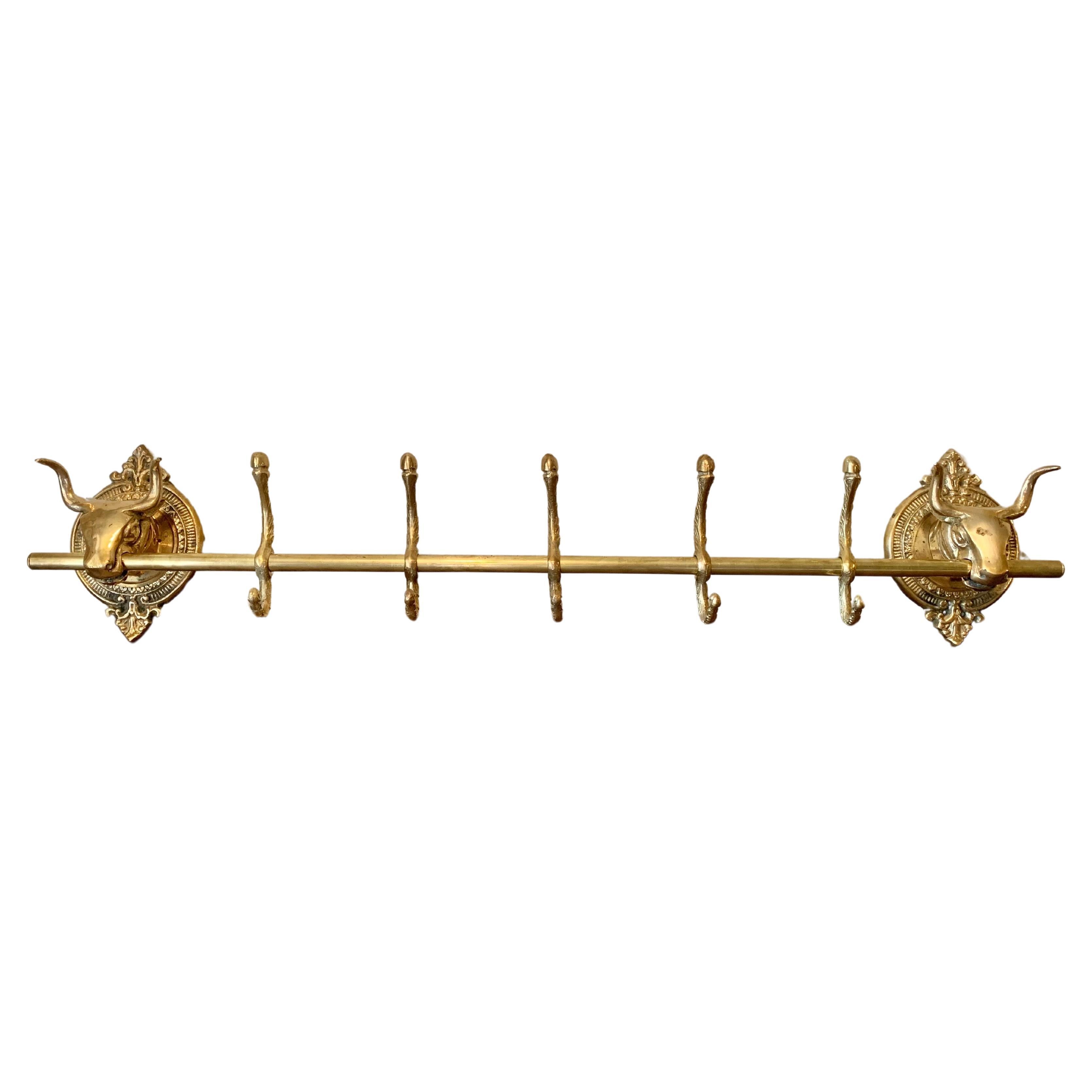 This large Mid 20th Century Longhorn Cow Head Coat or Hat Rack was crafted from brass in the mid 1900's. The piece features two cow heads mounted on intricately detailed oval brass plaques that are adjoined by a center rod containing five hooks.