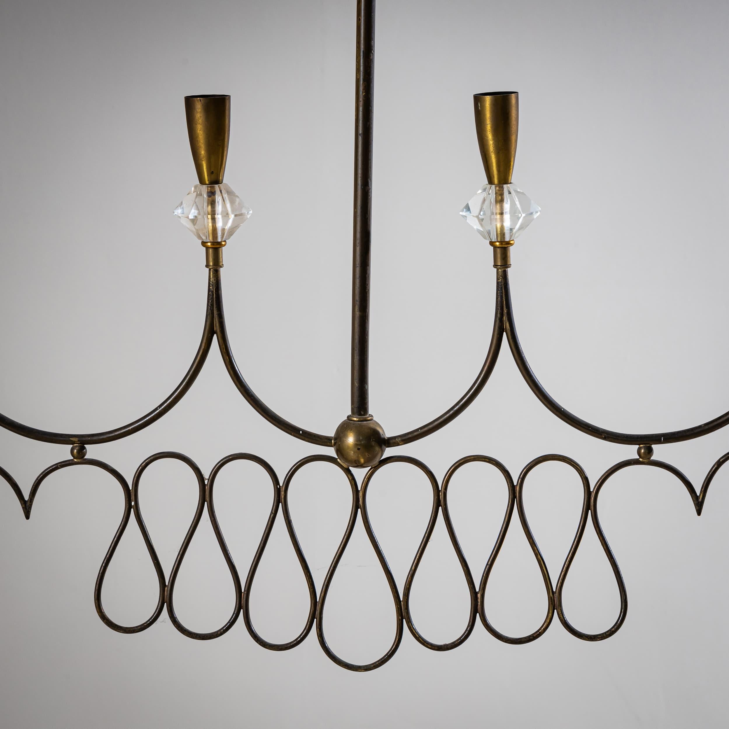 Elegant pendant lamp featuring six sockets, adorned with glass prisms and a looped brass design. Its slim, horizontal profile makes it especially well-suited for dining area installations. A refined example of 1950s Italian lighting design.