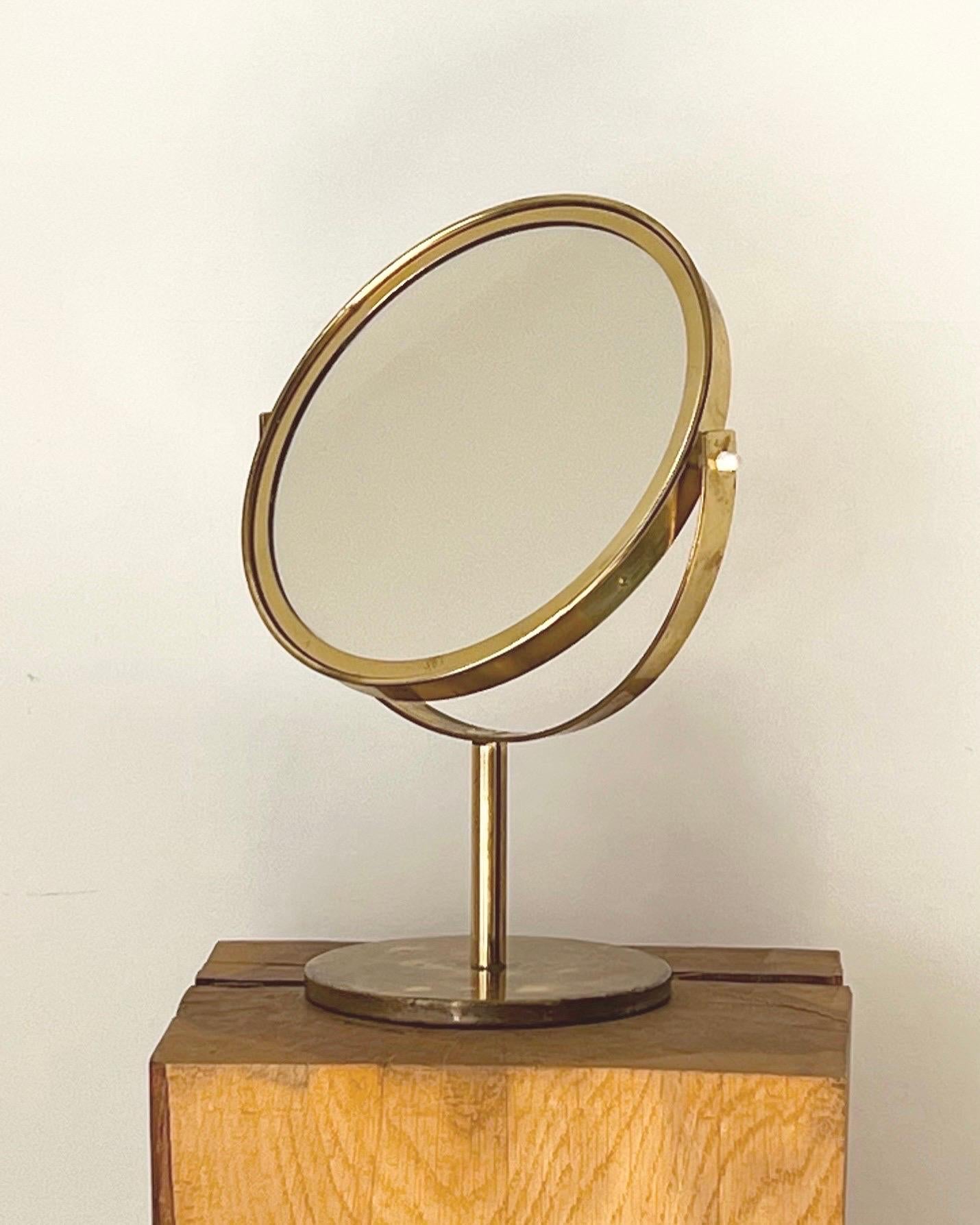A double-sided brass table mirror by Hans Agne-Jakobsson, Mid-20th century, Sweden. Full size reflecting mirror to one side, and smaller magnifying mirror the to the reverse. The mirror turns left/right through the stem and the tilt can be adjusted