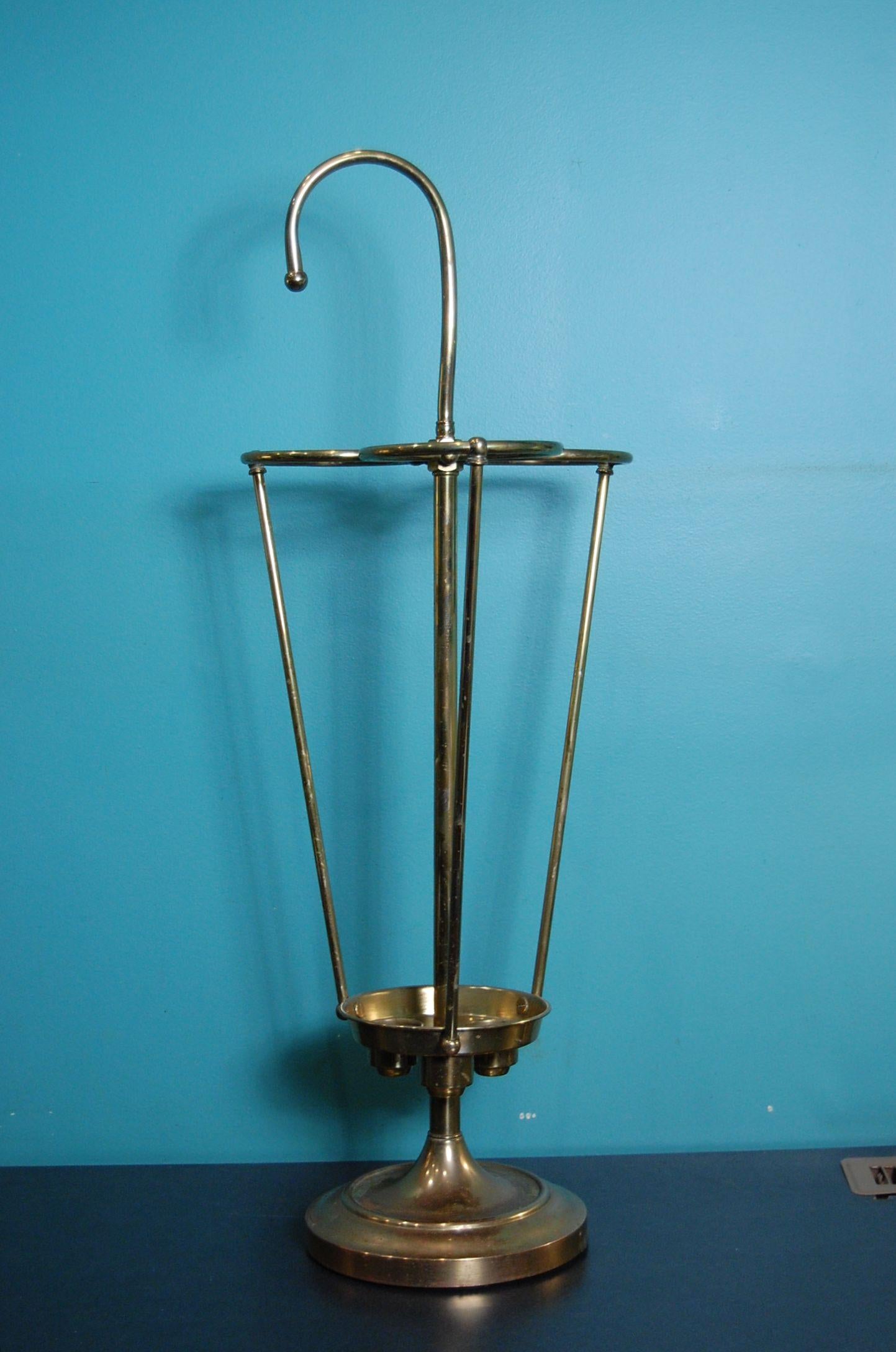 A brass umbrella Stand by the Herco Art Manufacturing Company in solid tubular construction holding three umbrellas (umbrellas not inc). The vertical posts, handle and three rings still retain much of the polished look, however the base has