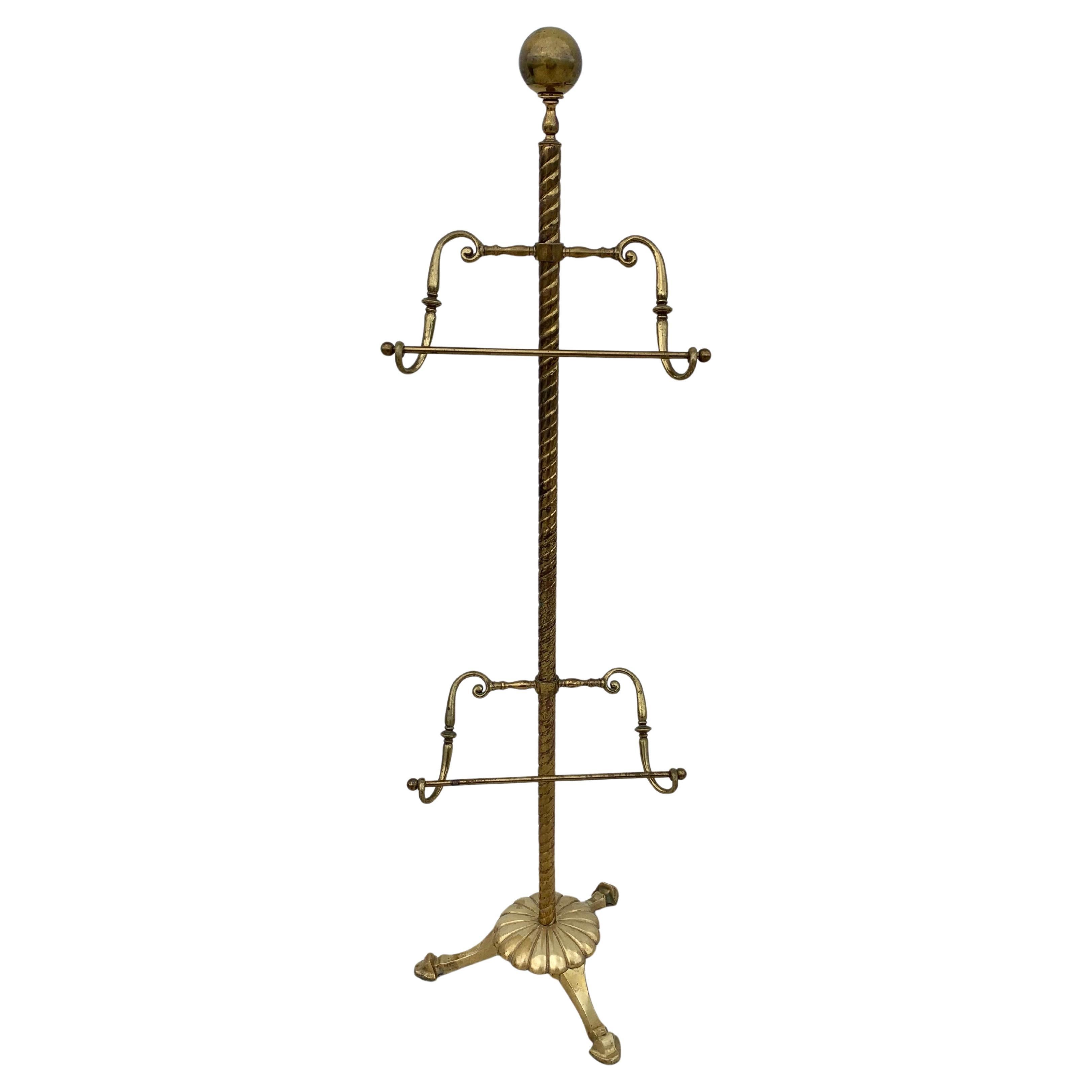 This Mid 20th Century Valet Stand was crafted from brass in the mid 1900's. Often called a silent butler, the piece displays cast brass details with a seasoned patina. Featuring a spherical finial above two adjustable racks that are flanked by