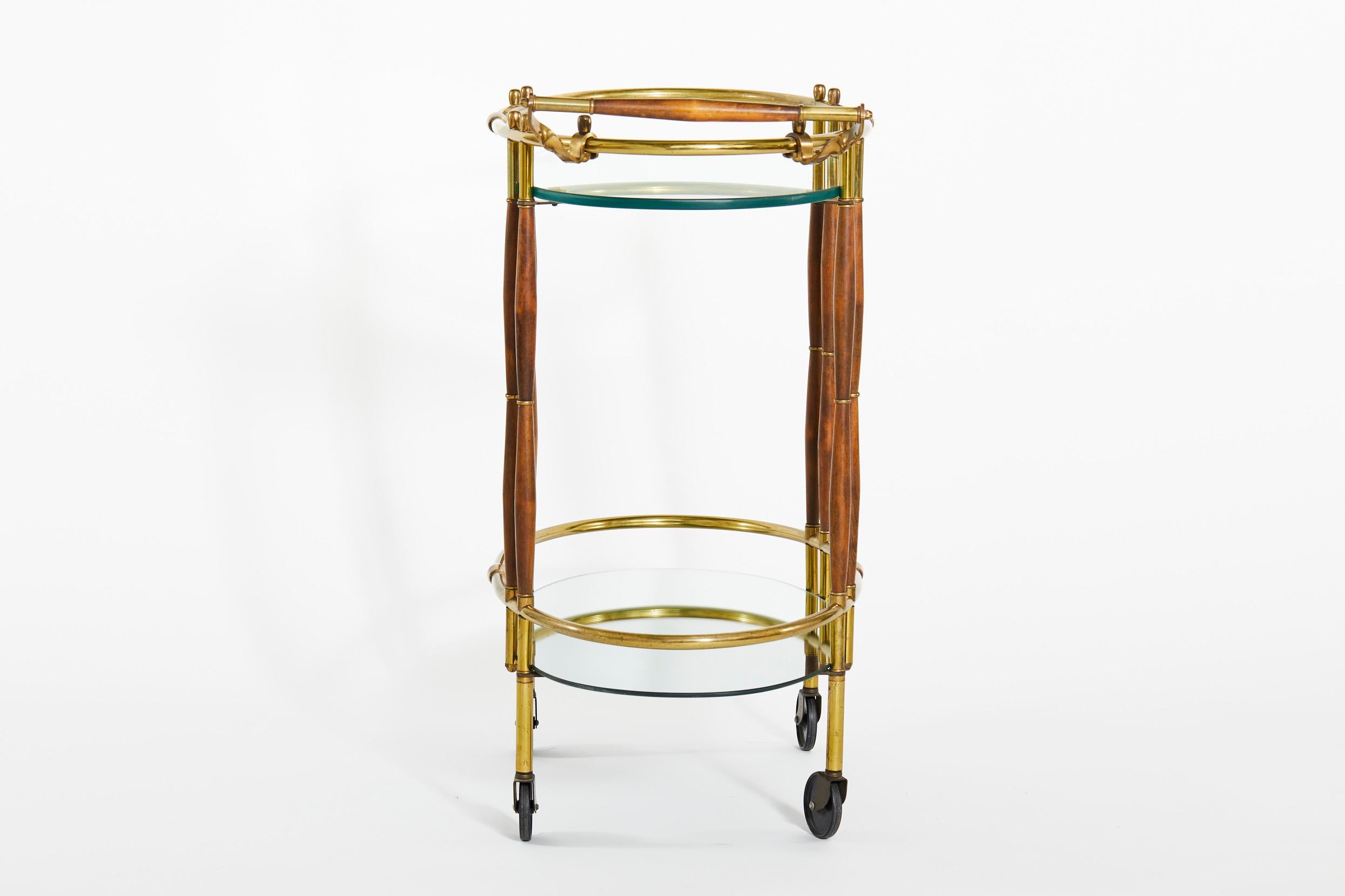 Beautiful mid 20th century brass frame with mahogany wood design details two tiered wheeled bar cart. The bar cart features very heavy glass shelve top, a lower mirrored shelve with side handle. The cart is in great condition. Minor wear consistent
