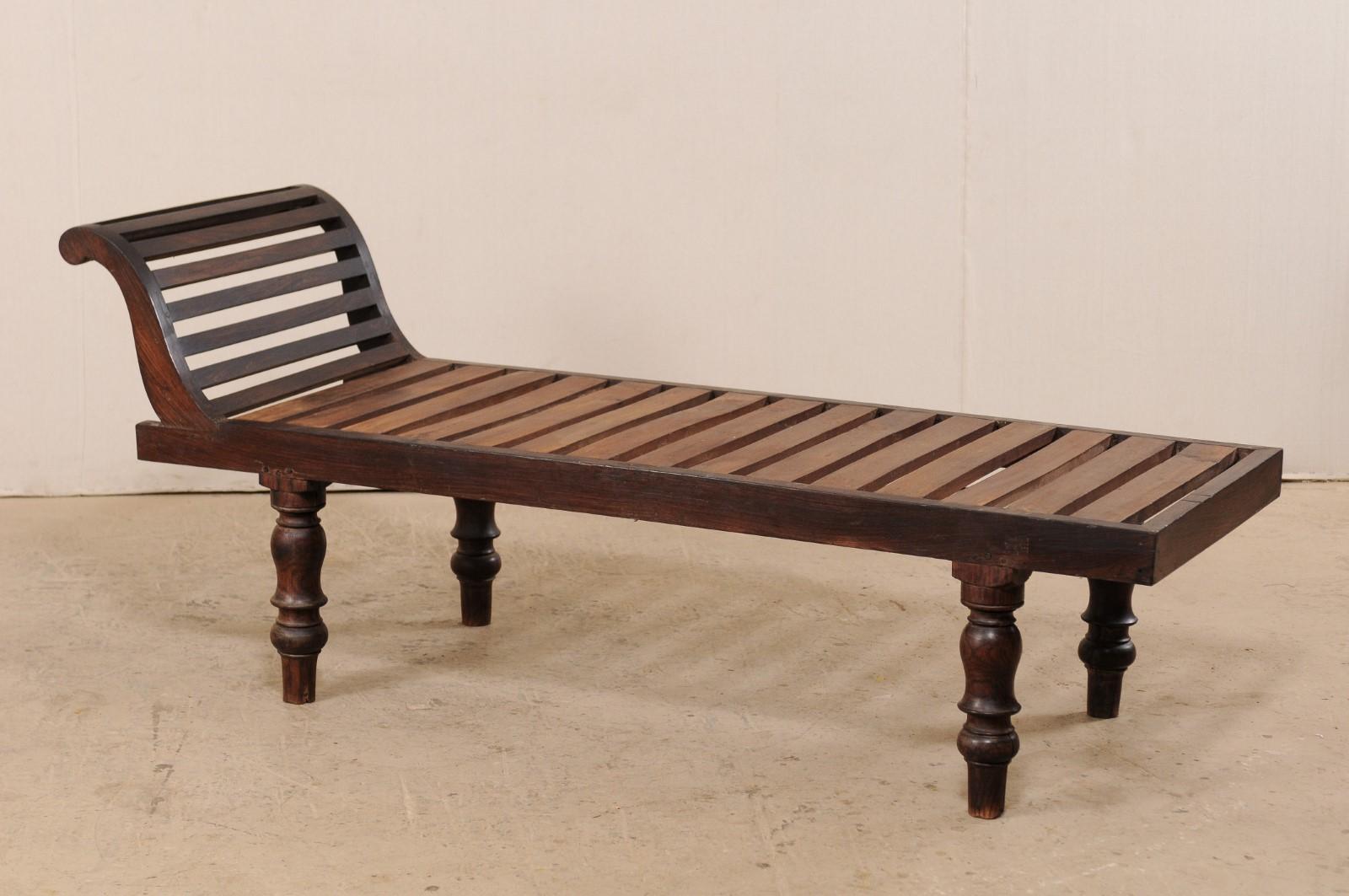 A British Colonial chaise lounge from the early to mid-20th century. This sleek Anglo-Indian lounging style daybed from India features a sturdy wooden constructed slat bed, with gracefully curved back rest, and is presented upon classic turned legs.