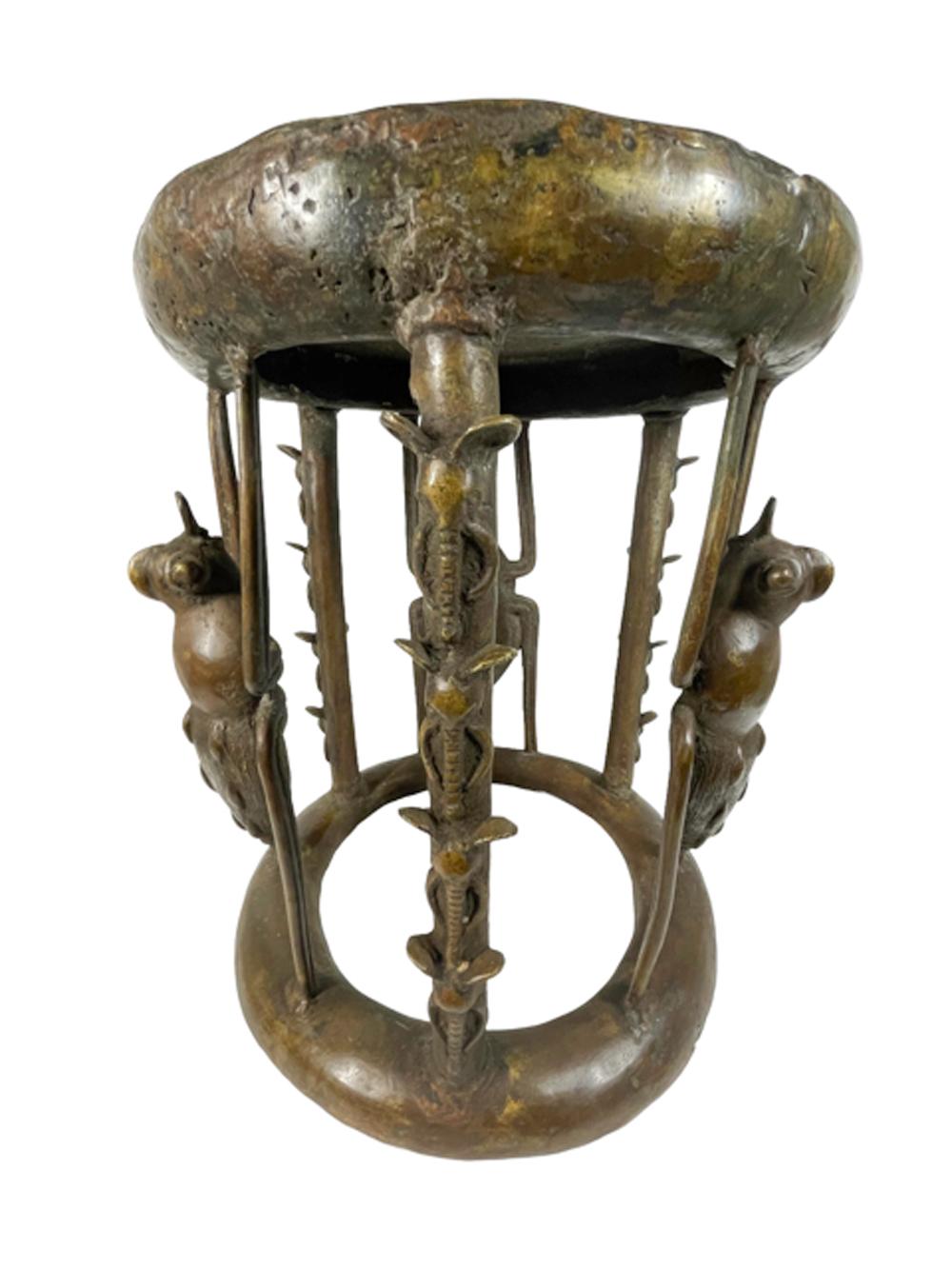 Bronze stool of cylindrical form with a cushion-form top on six supports of alternating posts with elephant heads between large outstretched beetles all rising from a convex circular foot. The top decorated with concentric circles of various