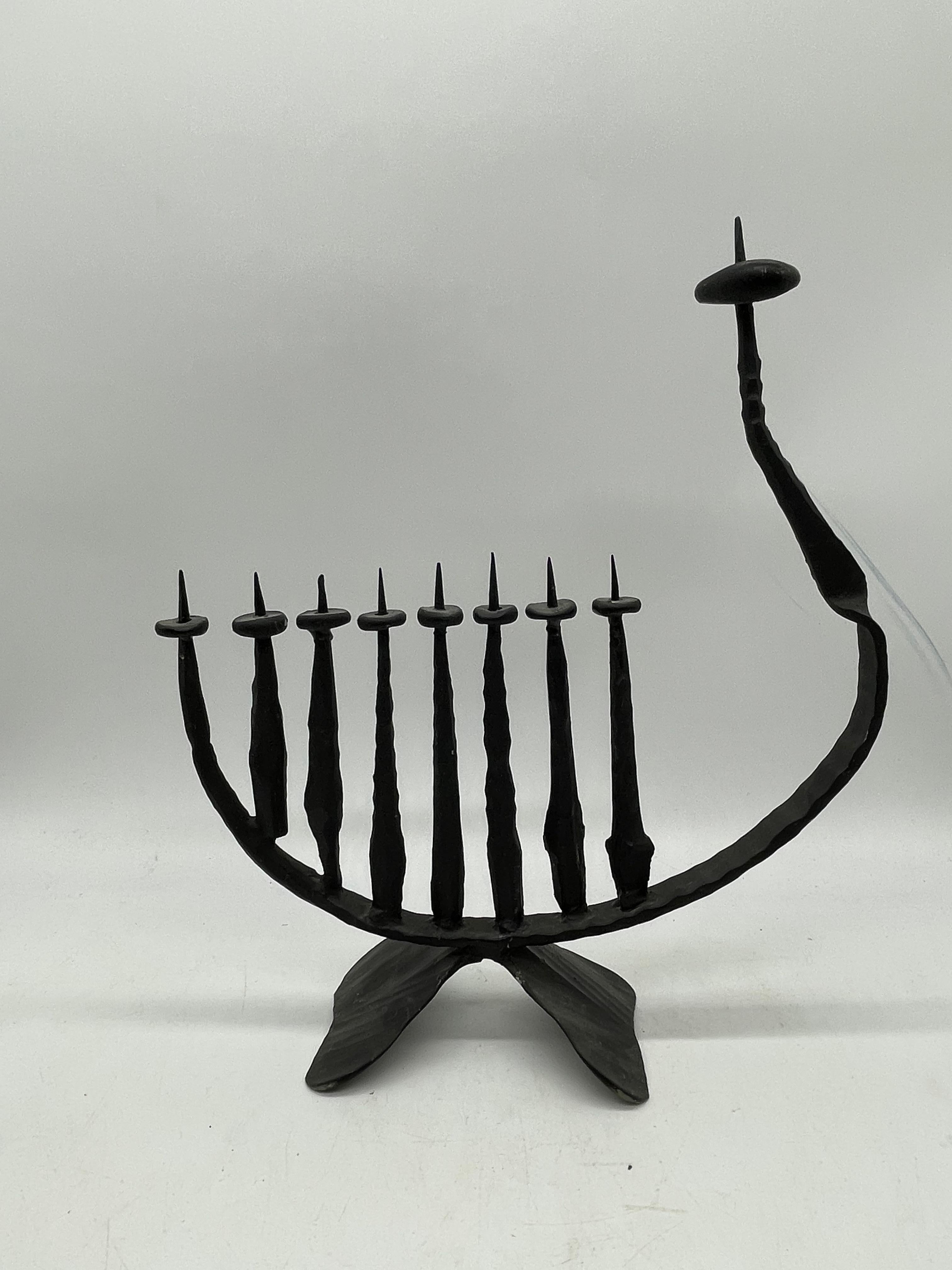 An impressive hand forged Hanukkah lamp inspired by Brutalist aesthetic. Hand crafted in Jerusalem, Israel circa 1960, the iron lamp stands with nine rustic candleholders in the shape of a harp. The shamash stands tallest in stature, featuring