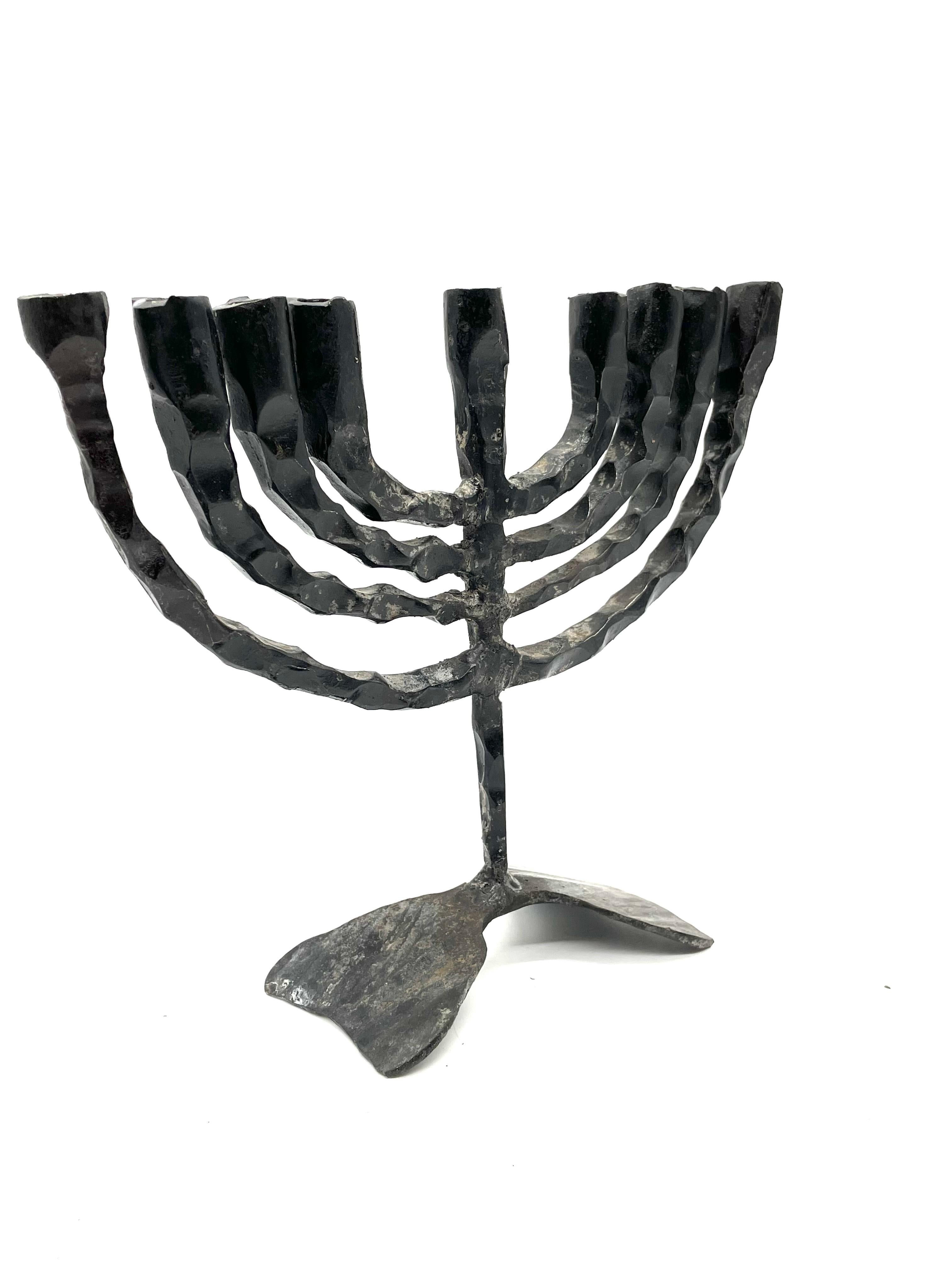 An impressive hand forged hanukkah lamp inspired by Brutalist aesthetic. Hand crafted in Jerusalem, Israel circa 1960, the iron lamp stands with nine rustic candleholders in traditional style. The middle candleholder, shamash, stands upright with