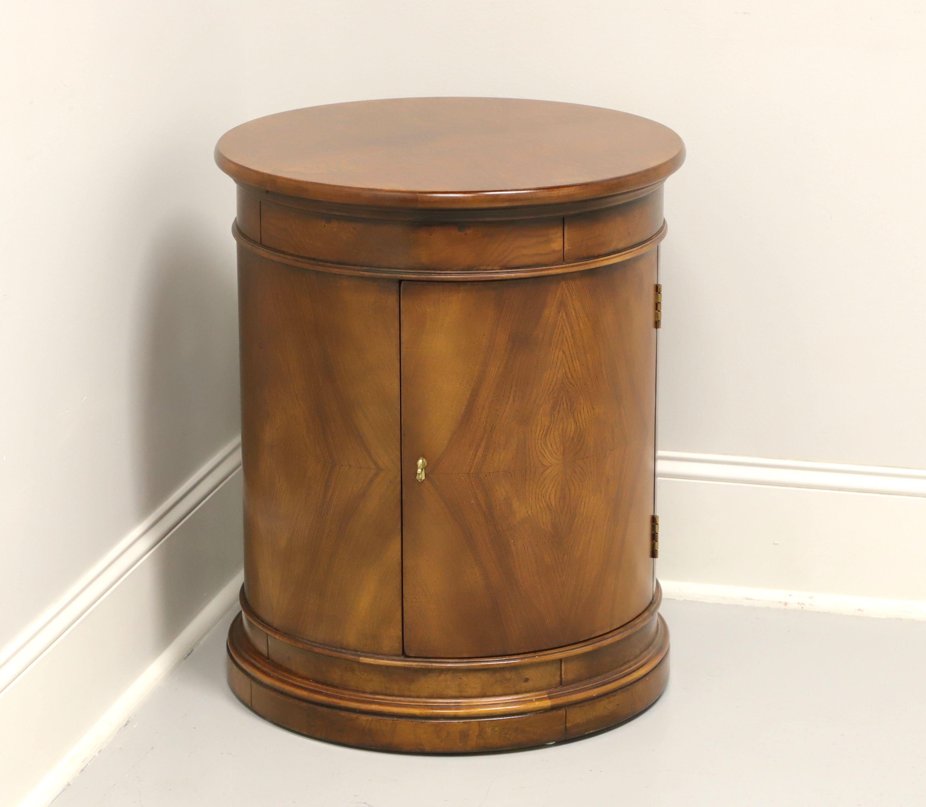 A Transitional style round cabinet accent table, unbranded, similar quality to Drexel or Henredon. Burl elm with brass hardware. Features burl top, bookmatched door front and ample storage within cabinet with one adjustable wood shelf. Made in the