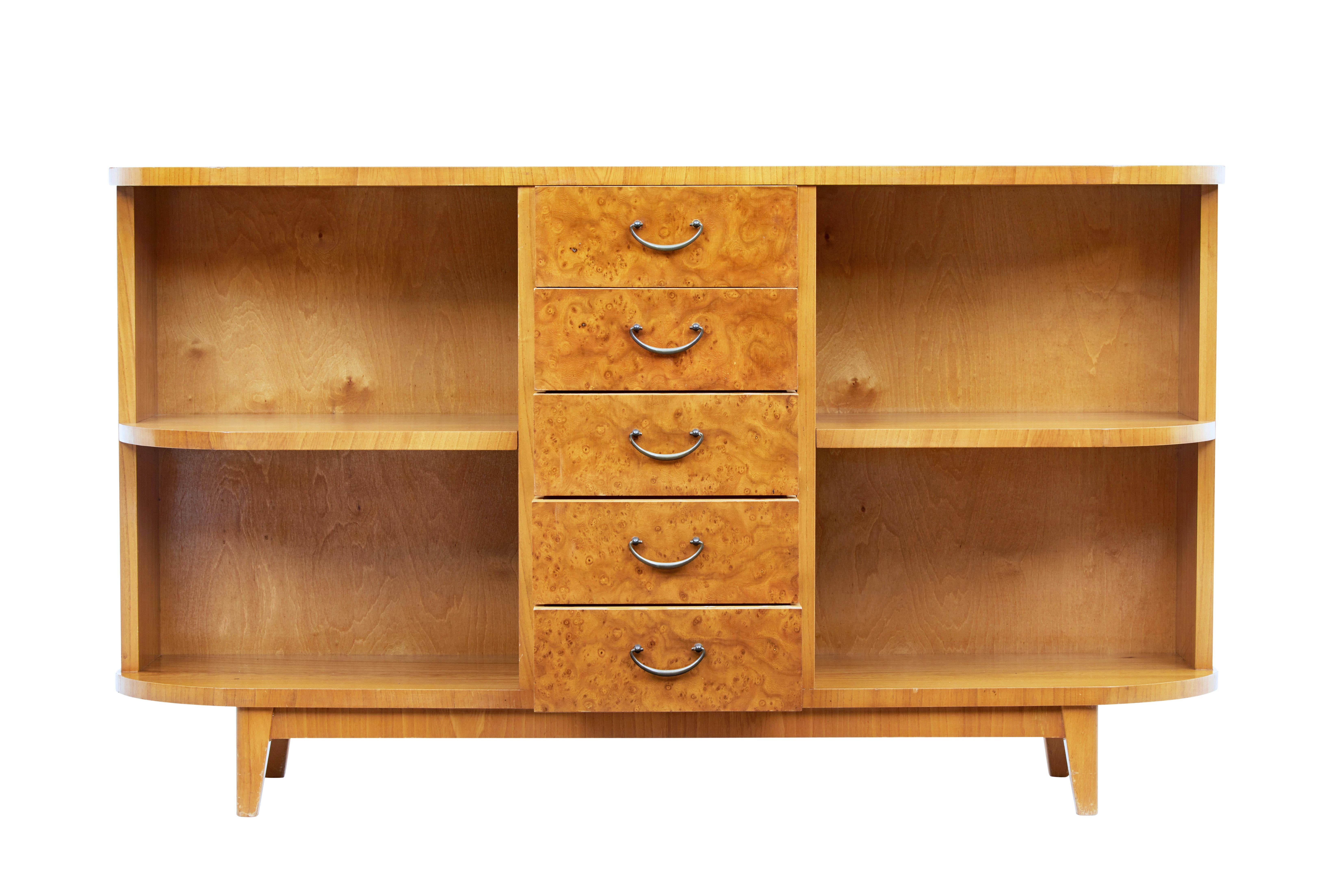 Good quality low open bookcase, circa 1940.

Central bank of 5 drawers veneered in burr birch and fitted with brass loop handles. Either side of the drawers are a single fixed shelf for book storage.

Rounded ends echo a influence from the art