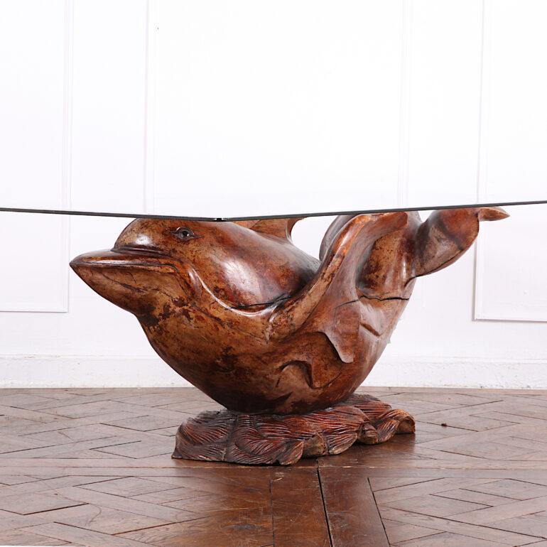 A hand-carved hardwood dolphin coffee table base signed A. Noll, the top supported on the uplifted tail and fins of the creature, who surfs on stylized carved waves.

Photographed with suitable / optional glass top- dimensions shown are wooden