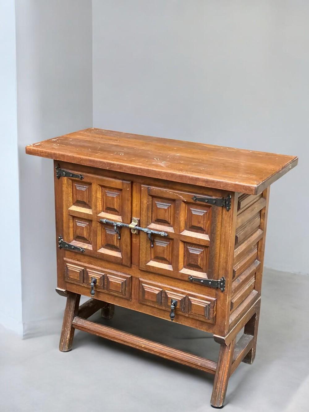 Dieser detailreiche Beistellschrank steht in der Tradition des Spanischen Revivals und zeichnet sich durch kühne Handwerkskunst und architektonische Präsenz aus. Das aus massiver Eiche gefertigte Möbelstück weist tief geschnitzte, geometrische