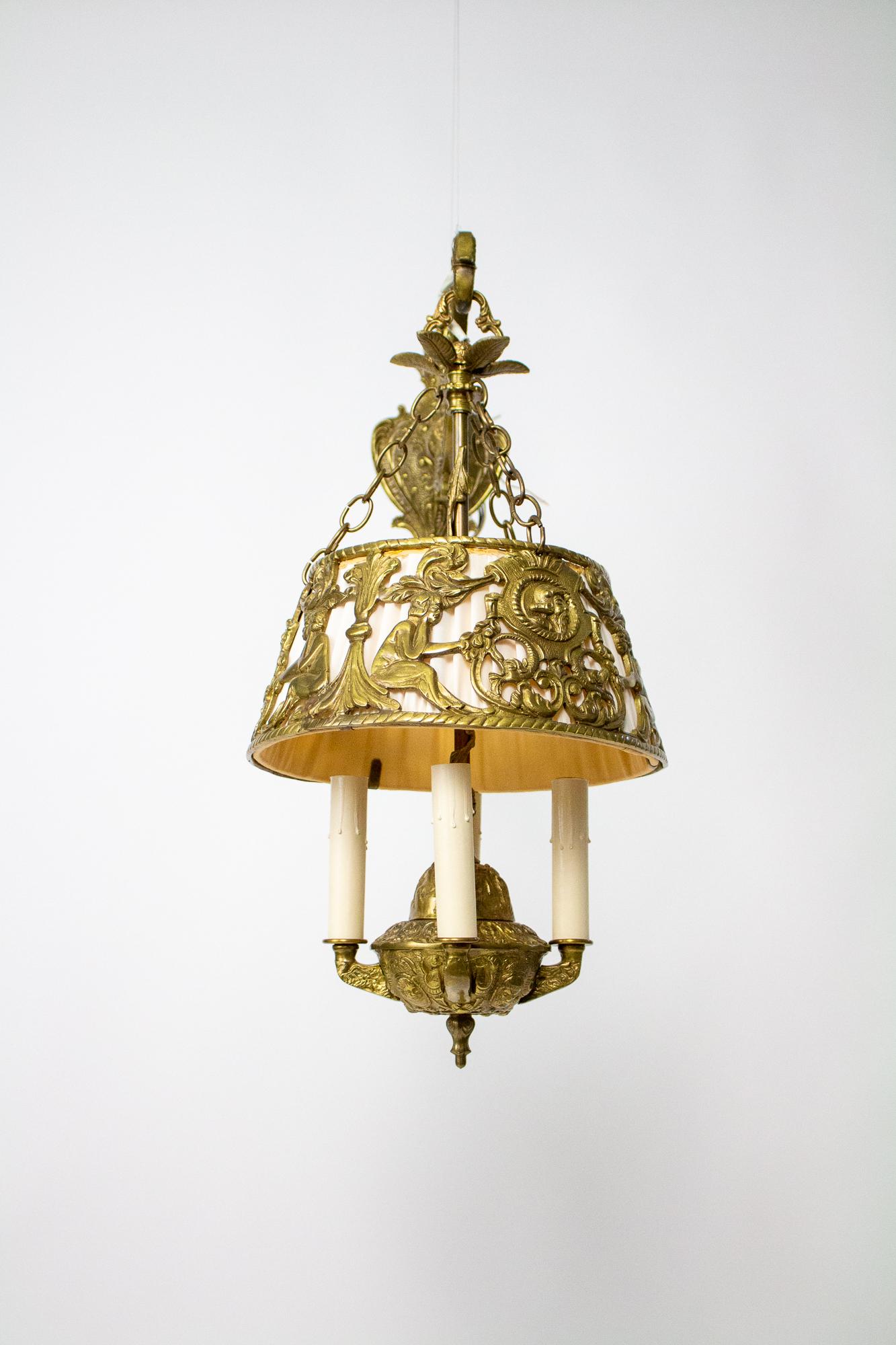 An unusual mid century maximalist hanging sconce. An ornate cast brass backplate and arm holds a hanging fixture. The Fixture is in the shape of a traditional whale oil light. The shade is silk backing a cast brass frame carrying images of