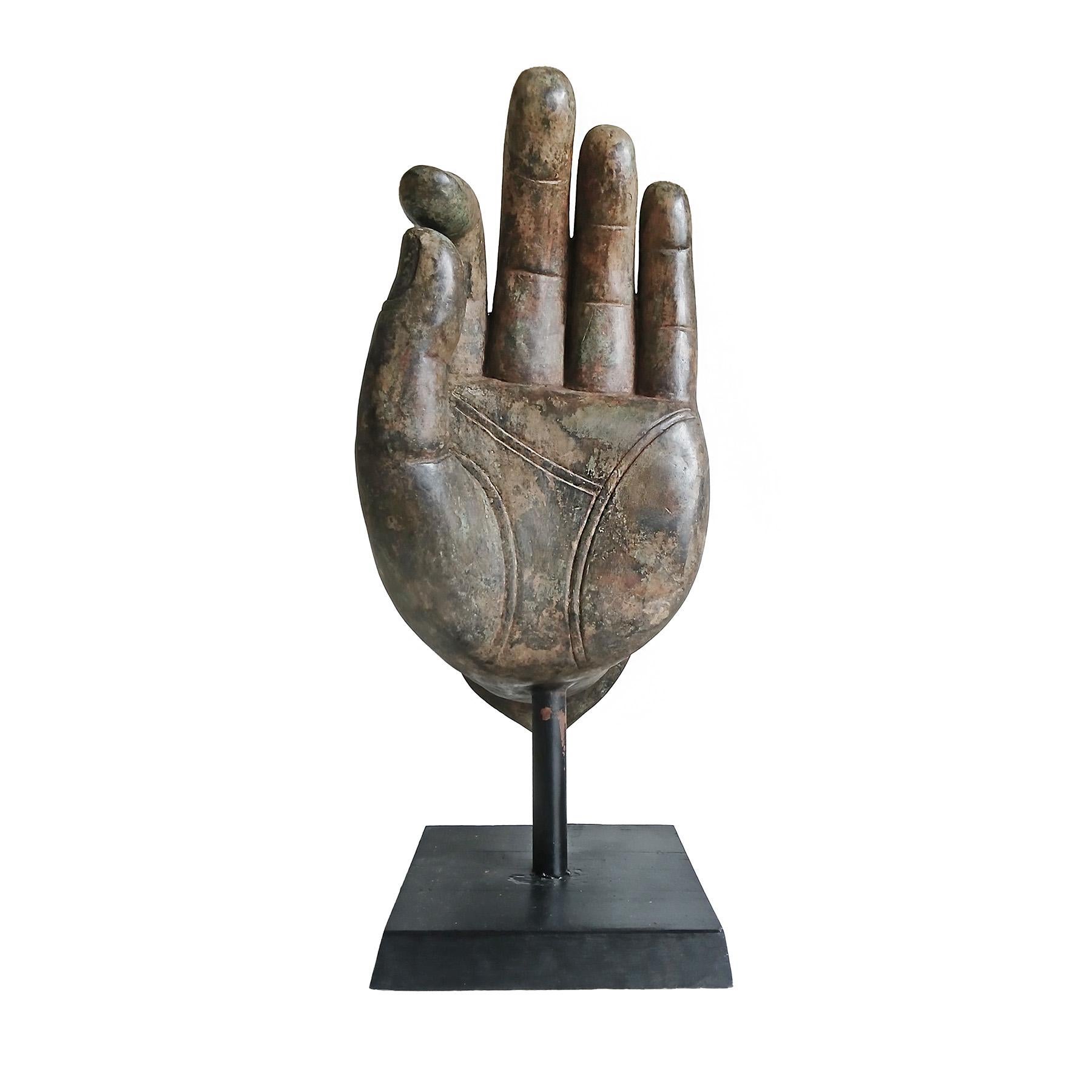 A large cast bronze sculpture of a Buddha's left hand, circa 1960. Mounted on a trapezoid-shaped wood and metal stand. 

The gesture is known as Dharmachakra Mudra, the traditional Buddhist gesture of teaching and discussion. This artistic