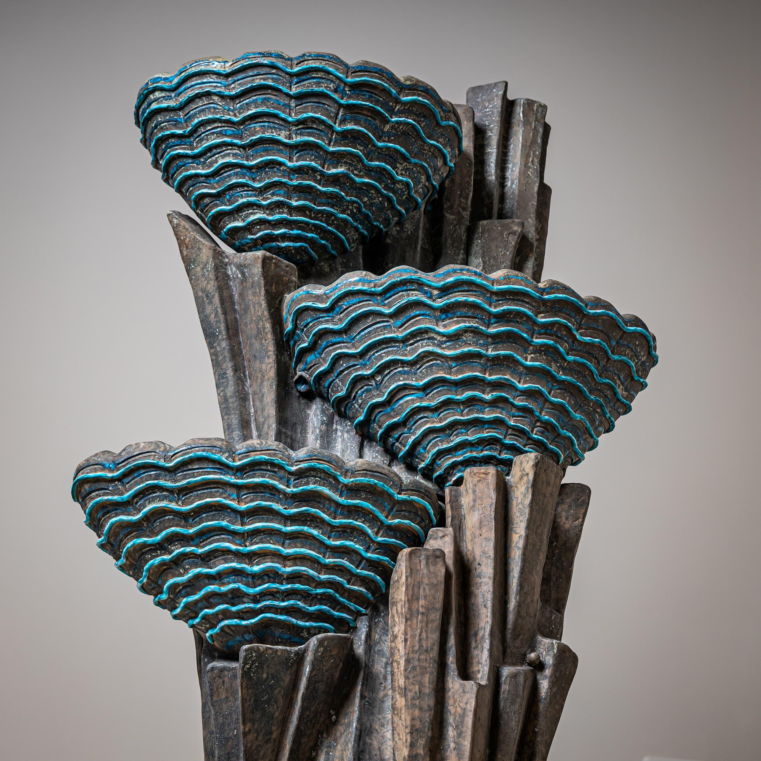Decorative three-tier indoor fountain made of glazed ceramic in shades of gray and turquoise, likely produced in the San Polo district of Venice. The cascading basins are shaped like scallop shells and set against a stylized rock formation. A
