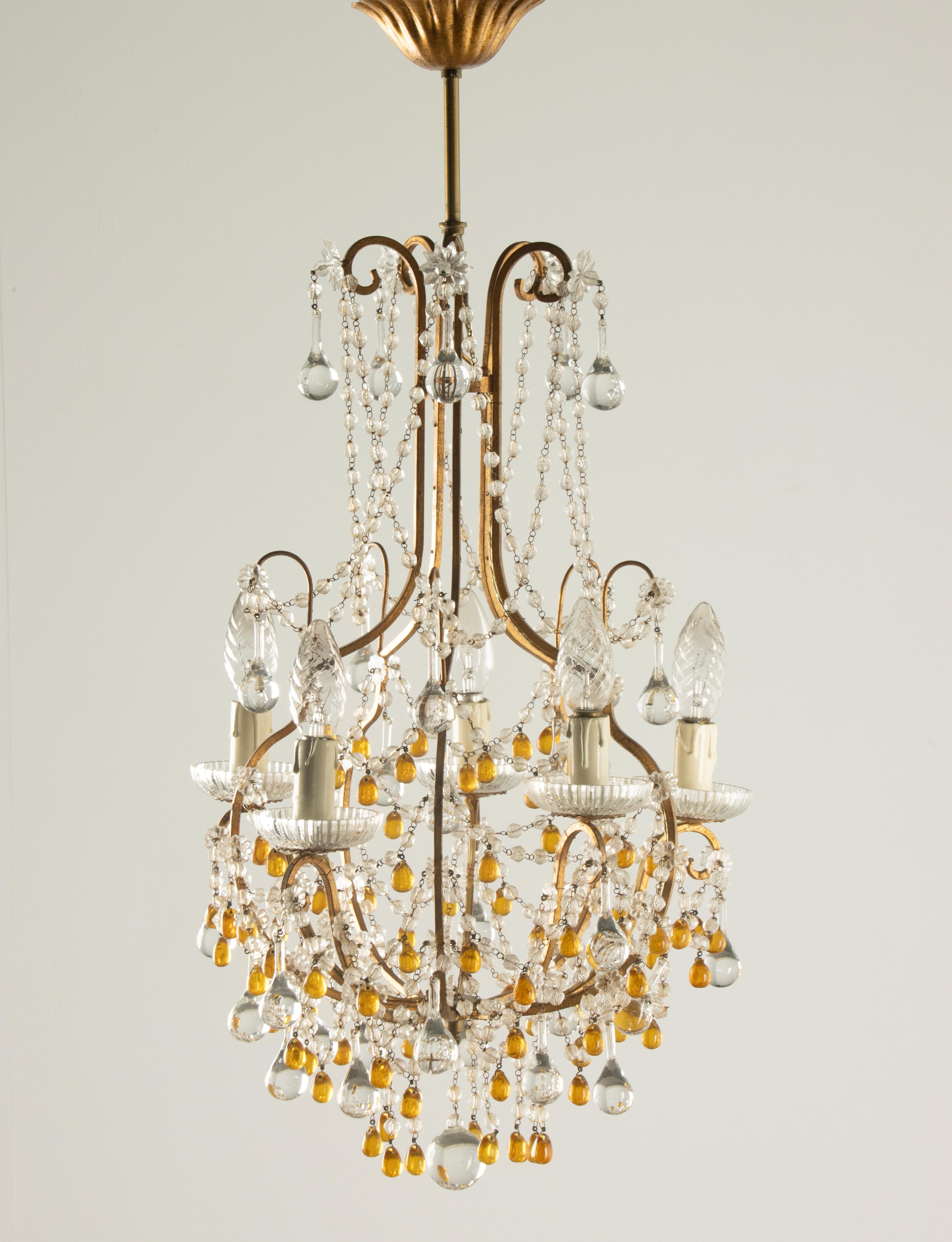 Elegante araña del siglo XX realizada en metal dorado y adornada con cuentas de cristal y gotas de vidrio ámbar. Esta refinada pieza presenta varios niveles de cadenas y colgantes de cristal, que crean un centelleante juego de luces. Los detalles en
