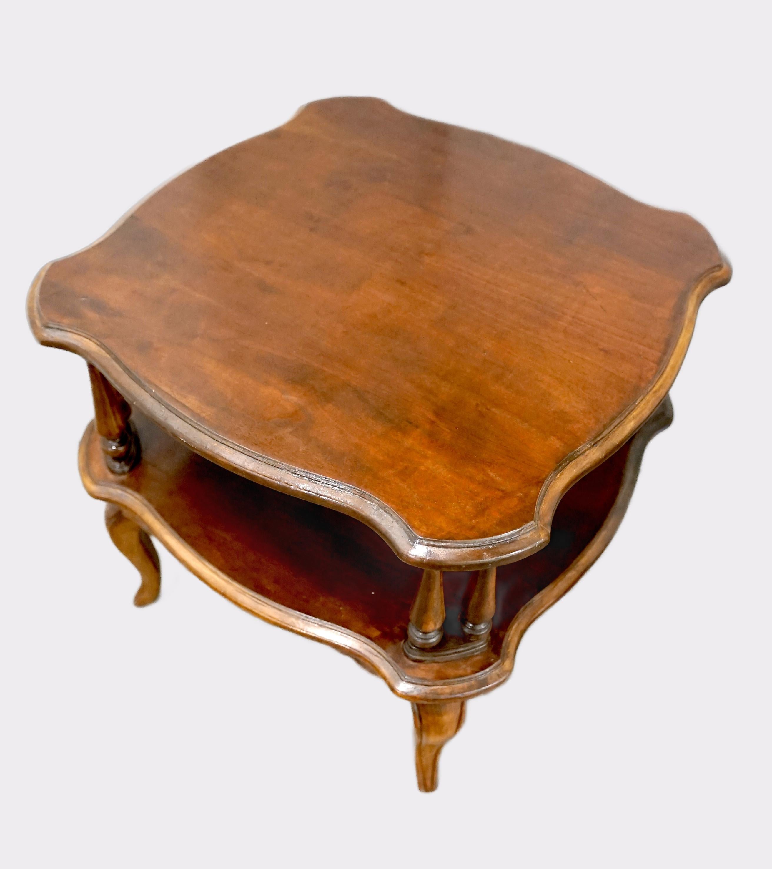 This table is a beautiful cherry wood two tier Queen Anne style piece. It has gently scalloped corners around the top and turned posts. This is a midcentury piece that has been refinished at some point in its history, but the table is solid and