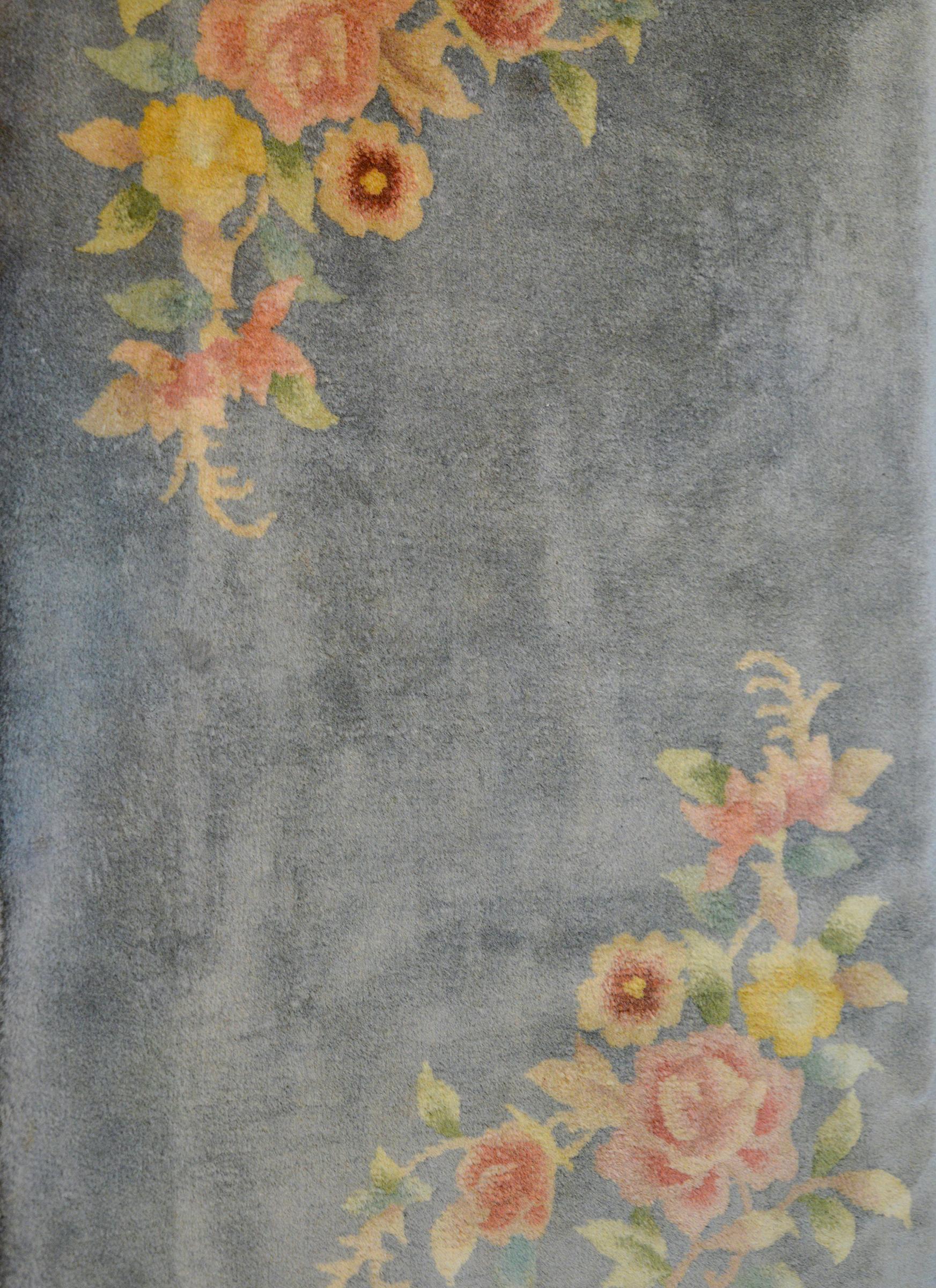Un adorable petit tapis Art déco chinois du milieu du 20e siècle avec un fond gris et des grappes de pivoines tissées en rose pâle, jaune, vert et bleu vivant dans les coins opposés.
