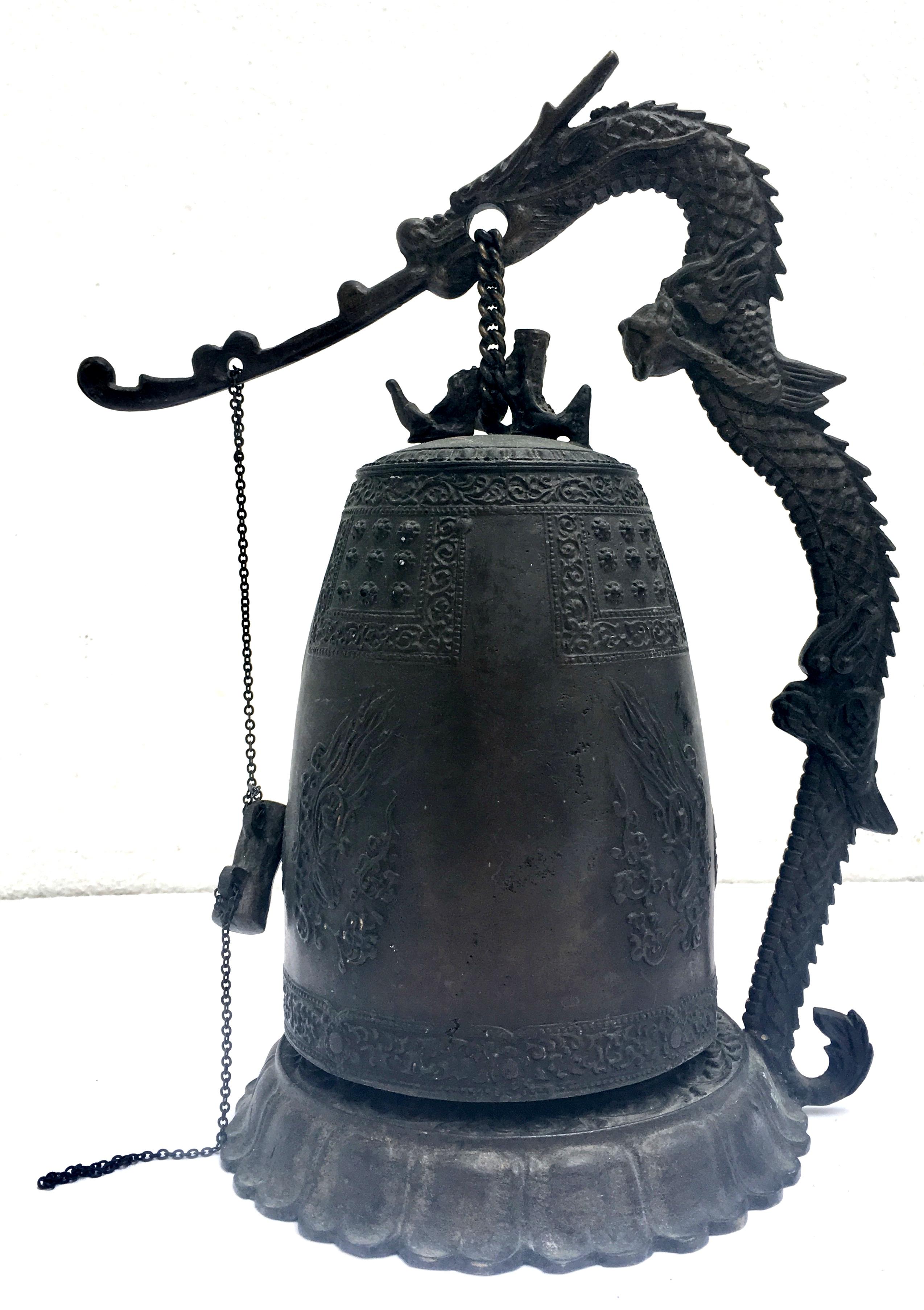 20th century antique bronze patina Chinese dragon gong bell with built in stand. Deeply embossed this solid bronze, traditional Chinese dragon bell features a swinging external clapper and abstract carved and curved dragon motif handle. The bell has