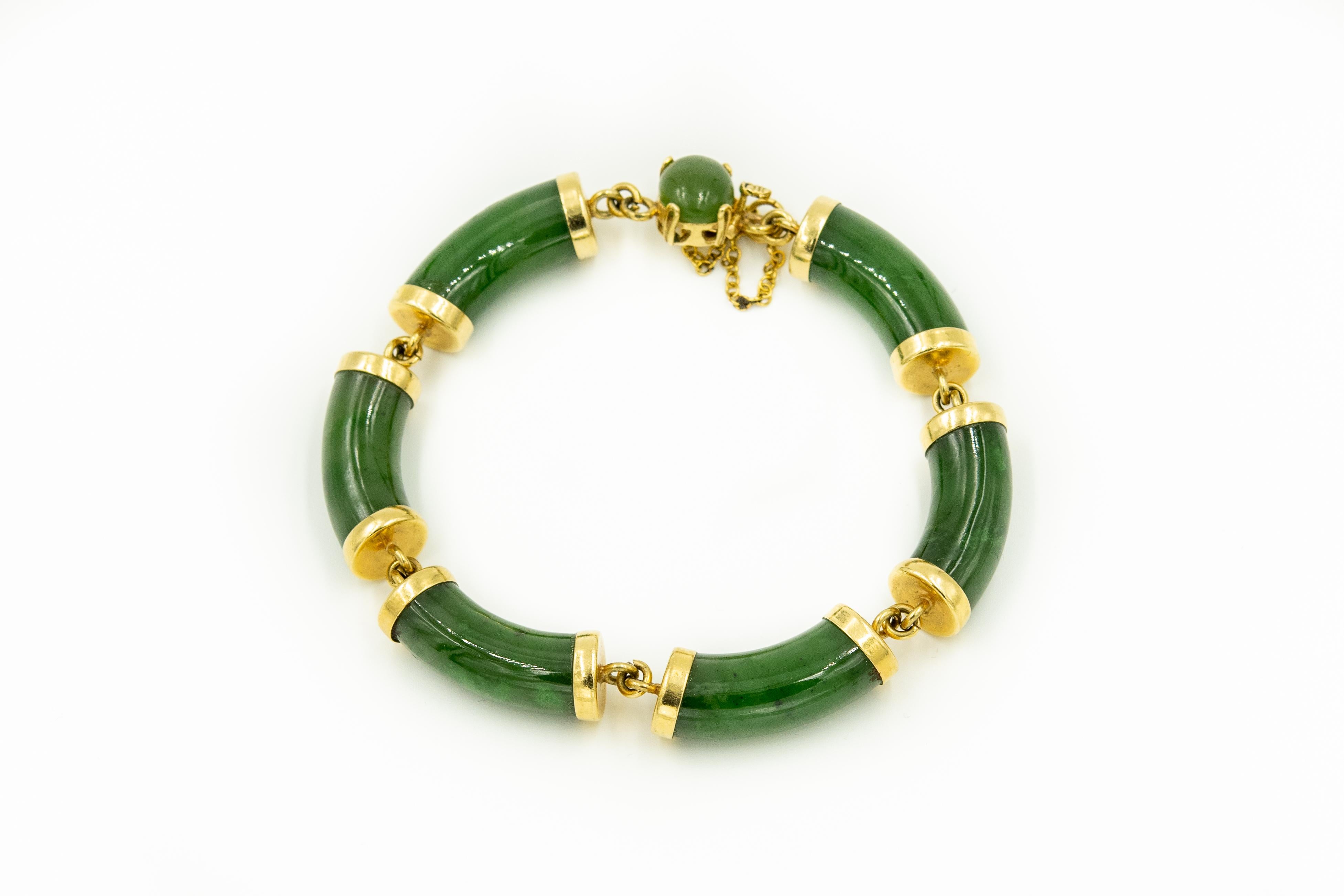 Chinese 14k yellow gold bracelet featuring nephrite jade bamboo bars with gold caps and matching clasp with an oval cabochon piece of jade on top of a 14k push button clasp.  The bracelet has an additional safety chain clasp bracelet.