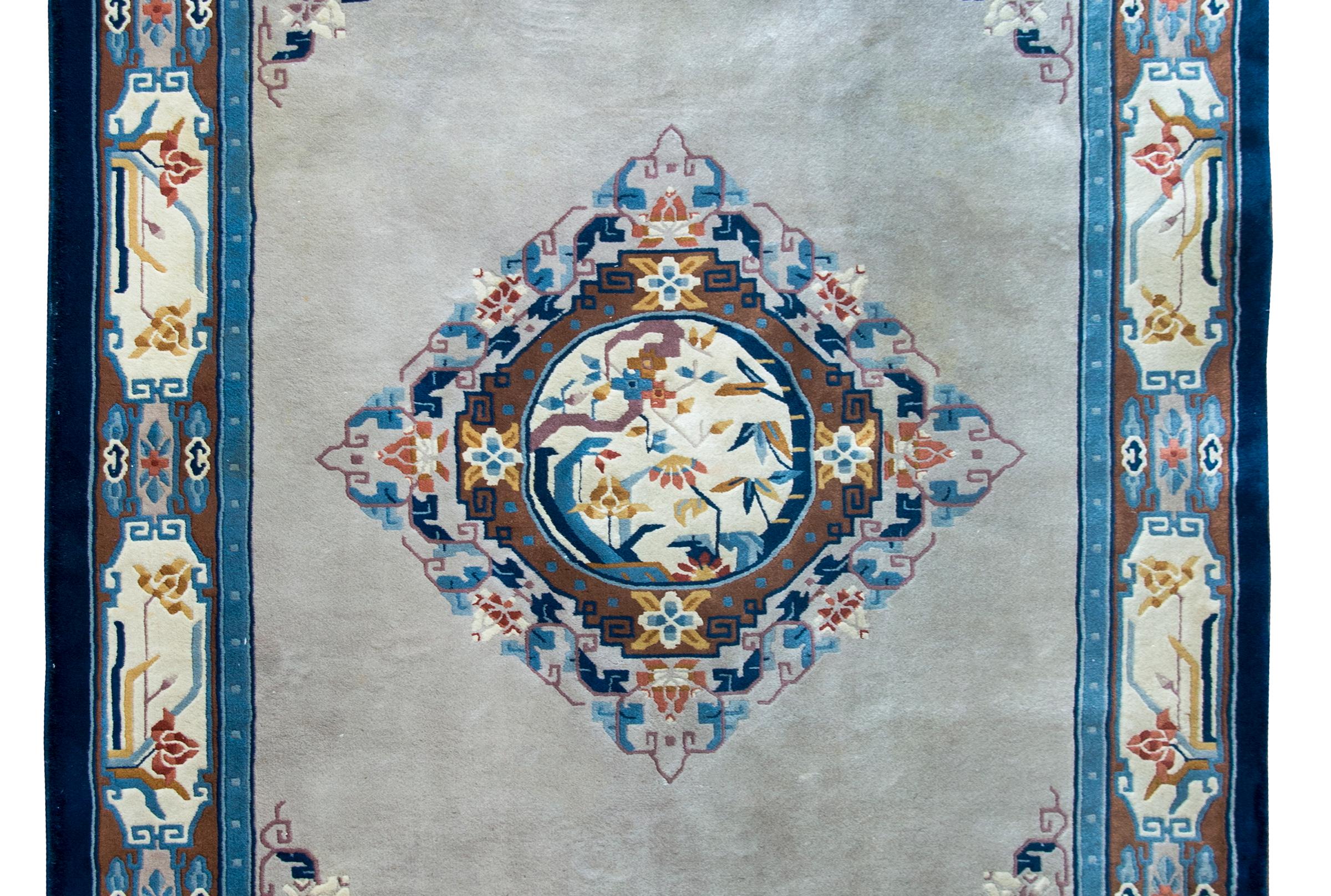 A brilliant mid-20th century Chinese hand-knotted wool rug with a central floral medallion with lotus flowers, bamboo leaves, and flowering prunus blossoms, surrounded by more stylized flowers, and living on a solid gray field with flowers in each