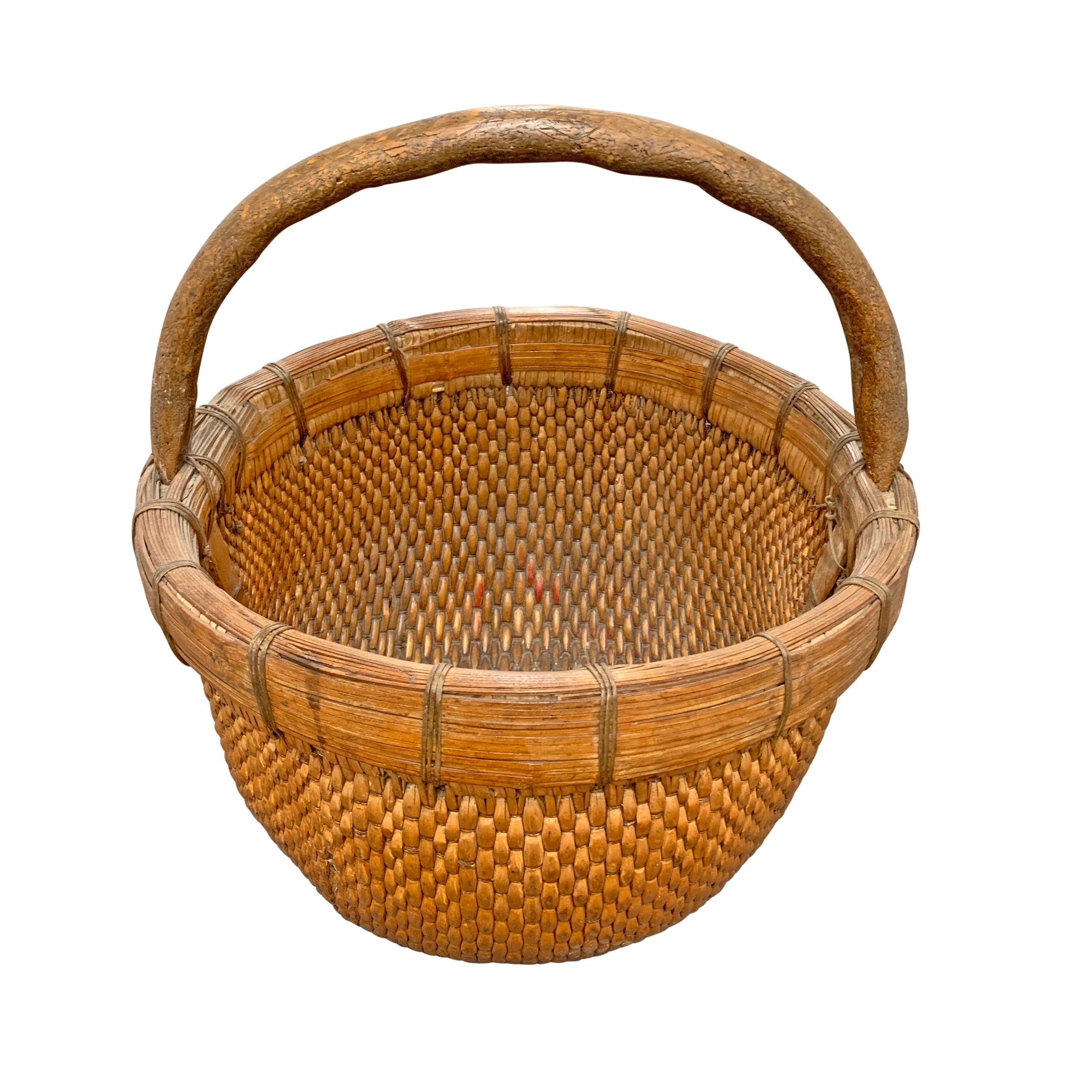 A mid-20th century Chinese woven reed gathering basket with a thick bentwood handle attached to a thick heavy band with woven reed lacing.