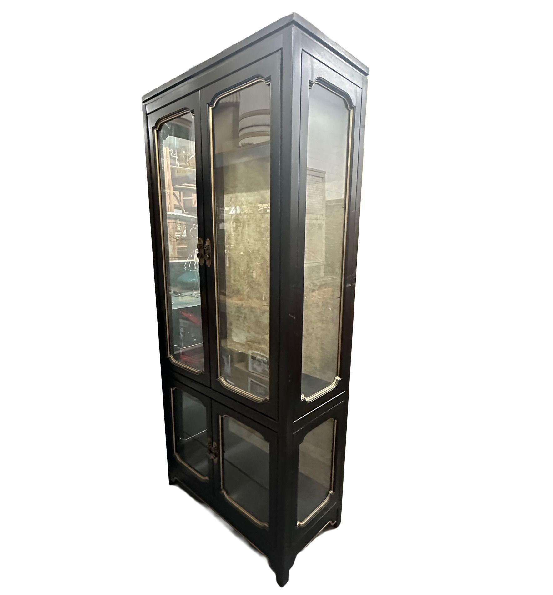 Presented here is an exquisite vintage chinoiserie-inspired illuminated display cabinet. Adorned with its original black finish complemented by elegant gold accents, this piece exudes timeless charm.

Illumination graces both the upper and lower