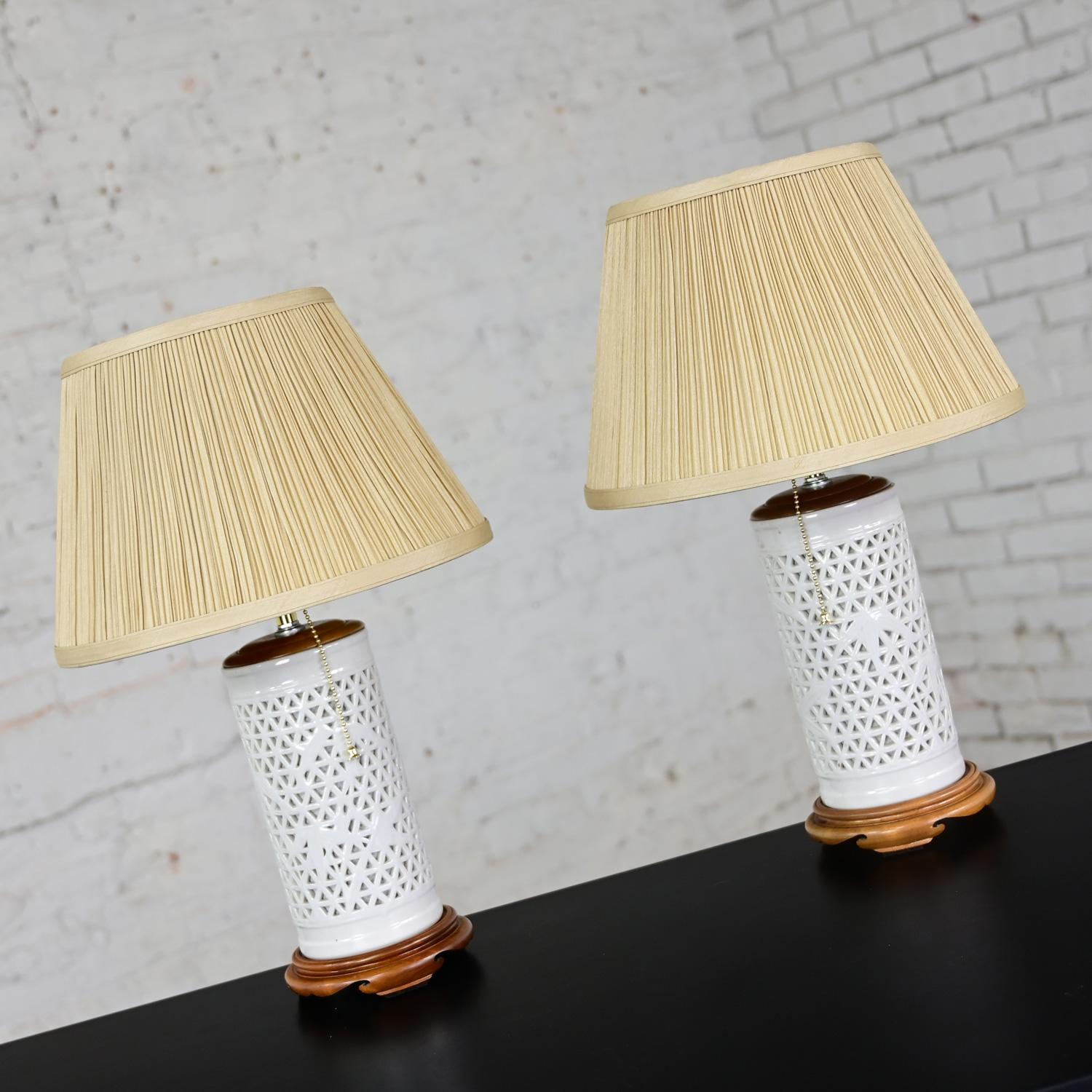 Impeccable Mid-20th Century Chinoiserie white pierced porcelain Blanc De Chine pair of lamps with new Ecru colored tapered & pleated silk-like shades with a hard paper inner liner, pull chain switch, and medium tone stained wood top & base.