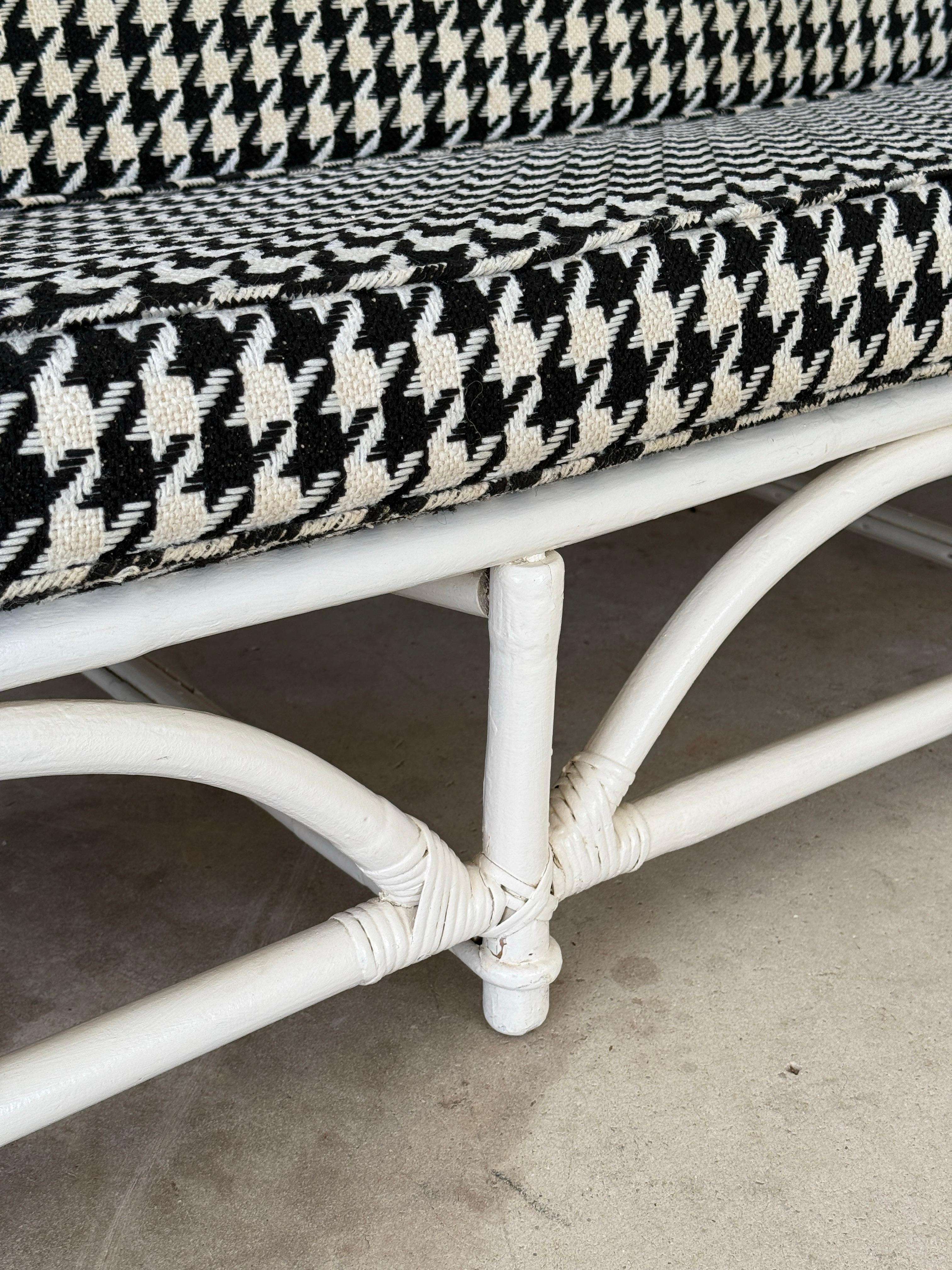 Classic bent rattan meets graphic drama in this Mid-20th Century three-seat rattan sofa by Ficks Reed. Featuring an arched apron design and curved rattan arms, the frame has been previously painted in white and shows signs of layered paint and