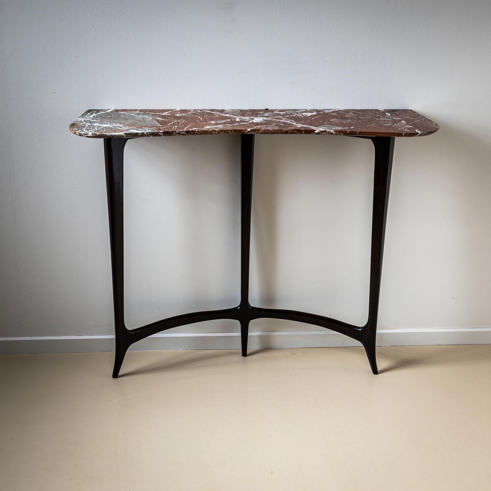 A striking 1940s Italian console table in the style of Guglielmo Ulrich, featuring a sleek ebonized three-legged frame. The narrow design is complemented by a stunning red marble top, distinguished by elegant white veining and a rounded, concave