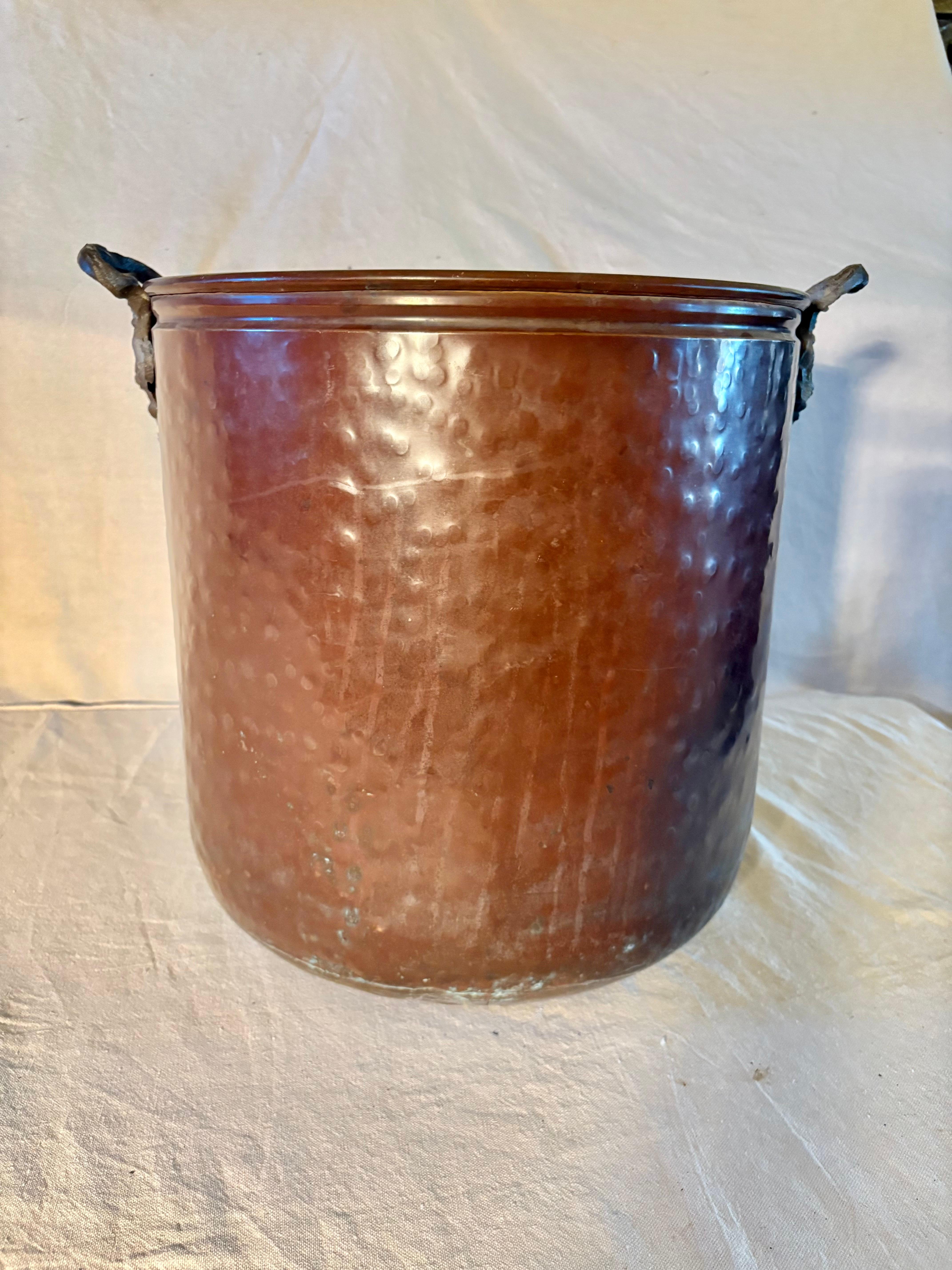Questo cachepot o secchiello della metà del XX secolo è stato realizzato in rame nella metà del 1900. Il pezzo è caratterizzato da due manici intricati e volumetrici attaccati da rivetti al corpo rotondo in rame martellato a mano. La parte superiore