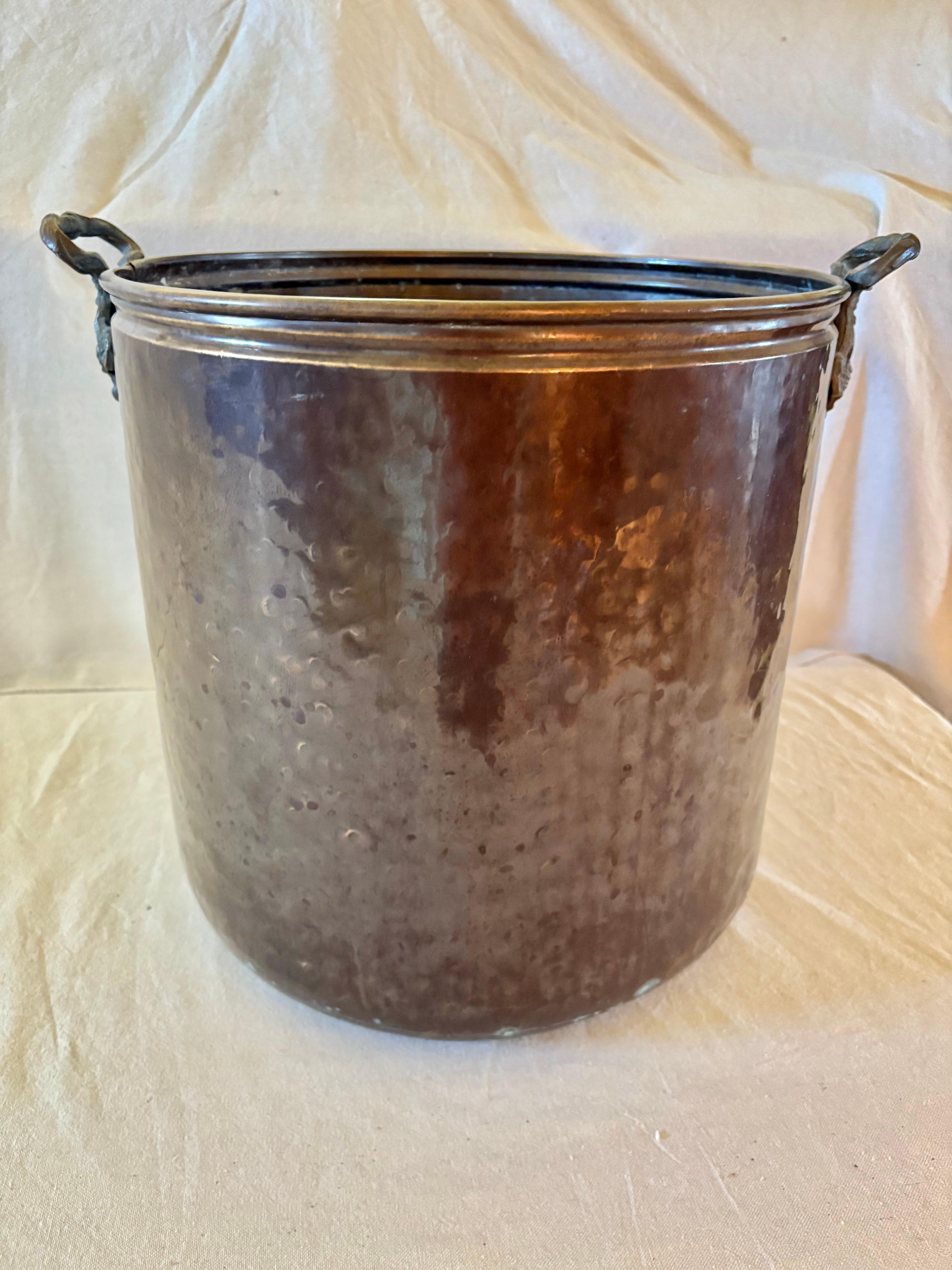 Questo cachepot o secchiello della metà del XX secolo è stato realizzato in rame nella metà del 1900. Il pezzo è caratterizzato da due manici intricati e volumetrici attaccati da rivetti al corpo rotondo in rame martellato a mano. La parte superiore