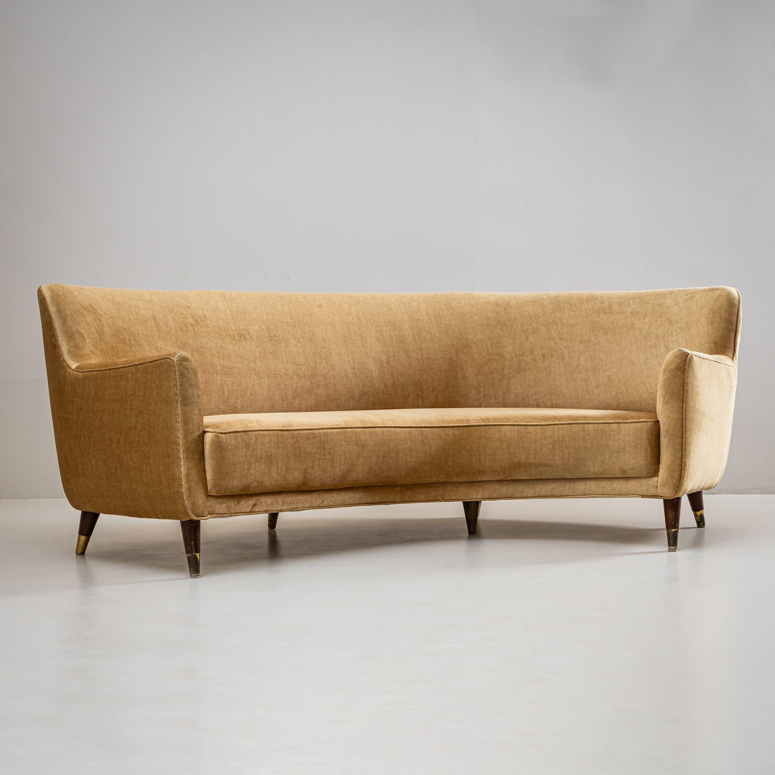 Elegante divano curvo disegnato da Gio Ponti negli anni Cinquanta. Il pezzo poggia su sette gambe affusolate con sabot in ottone ed è rivestito in un morbido tessuto giallo che accentua la sua forma scultorea e fluida. Accompagnato dal certificato