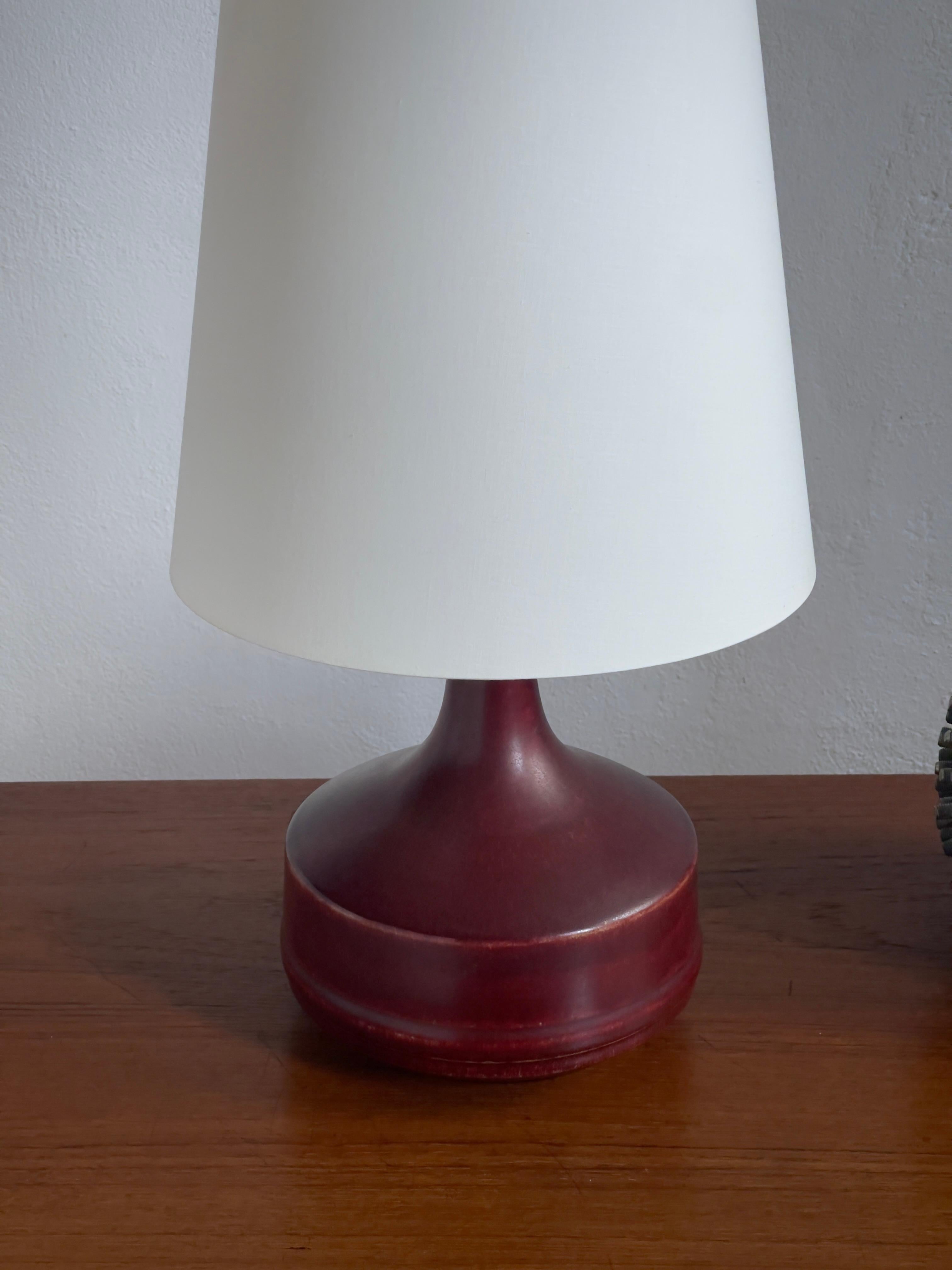 Cette lampe de table danoise en céramique du milieu du XXe siècle est un exemple frappant de l'art et de l'artisanat qui ont défini le design scandinave à cette époque. Sa riche glaçure oxblood, caractérisée par des tons rouges profonds et lustrés,
