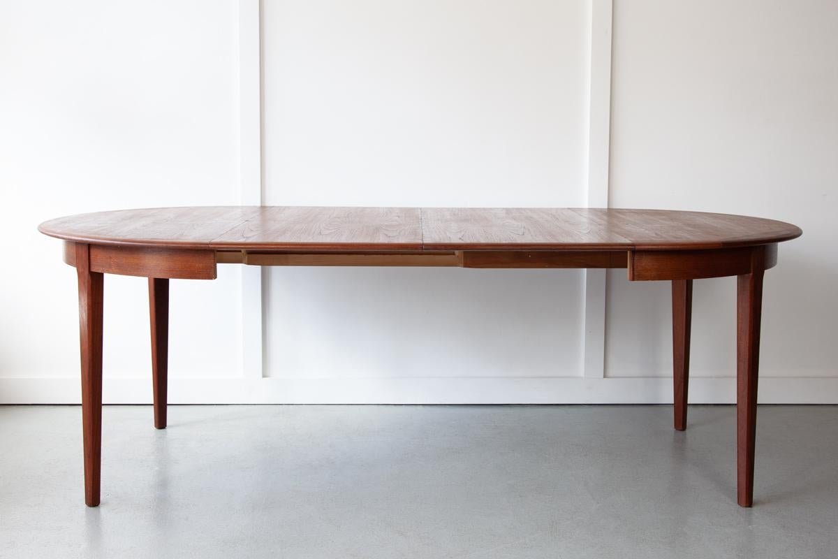 An extendable Danish dining table in teak with two separate leaves that slot in to extend the table to a generous sized oval. Standing on elegantly tapering legs and displaying clean lines, this dining table is a wonderful example of paired back,