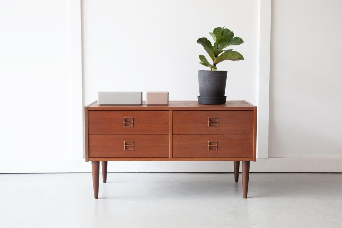 A lovely low chest of drawers in teak with classically midcentury inset handles and beautiful grain detailing, ideally sized for use as a television stand or media console. The simple design is pleasing, characterised by clean lines and the natural