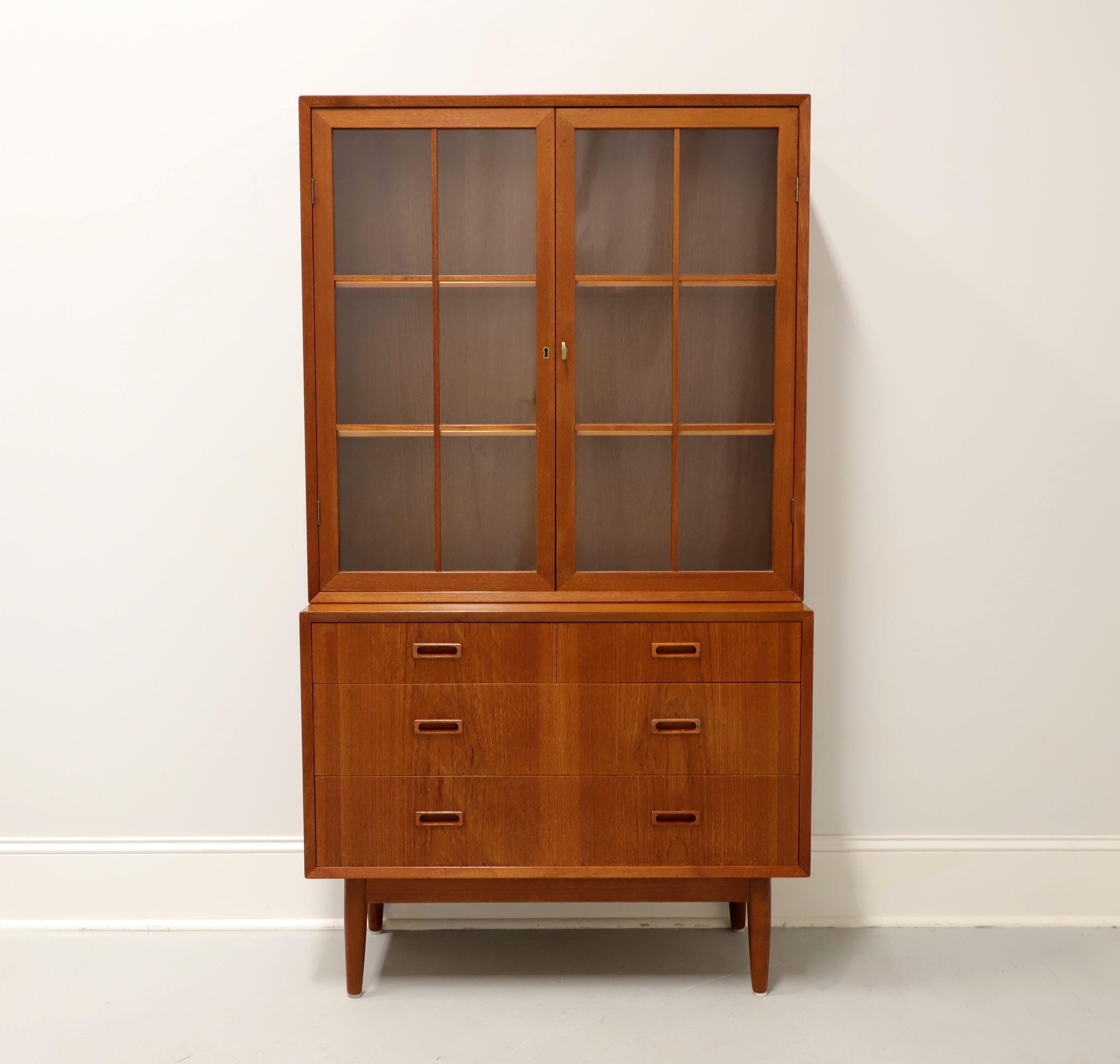 A Danish Modern style display cabinet, unbranded, similar in quality to Dyrlund or Skovby. Teak construction, step-back upper cabinet, squared modern design, elevated lower cabinet with apron and on round tapered legs. Upper cabinet has dual