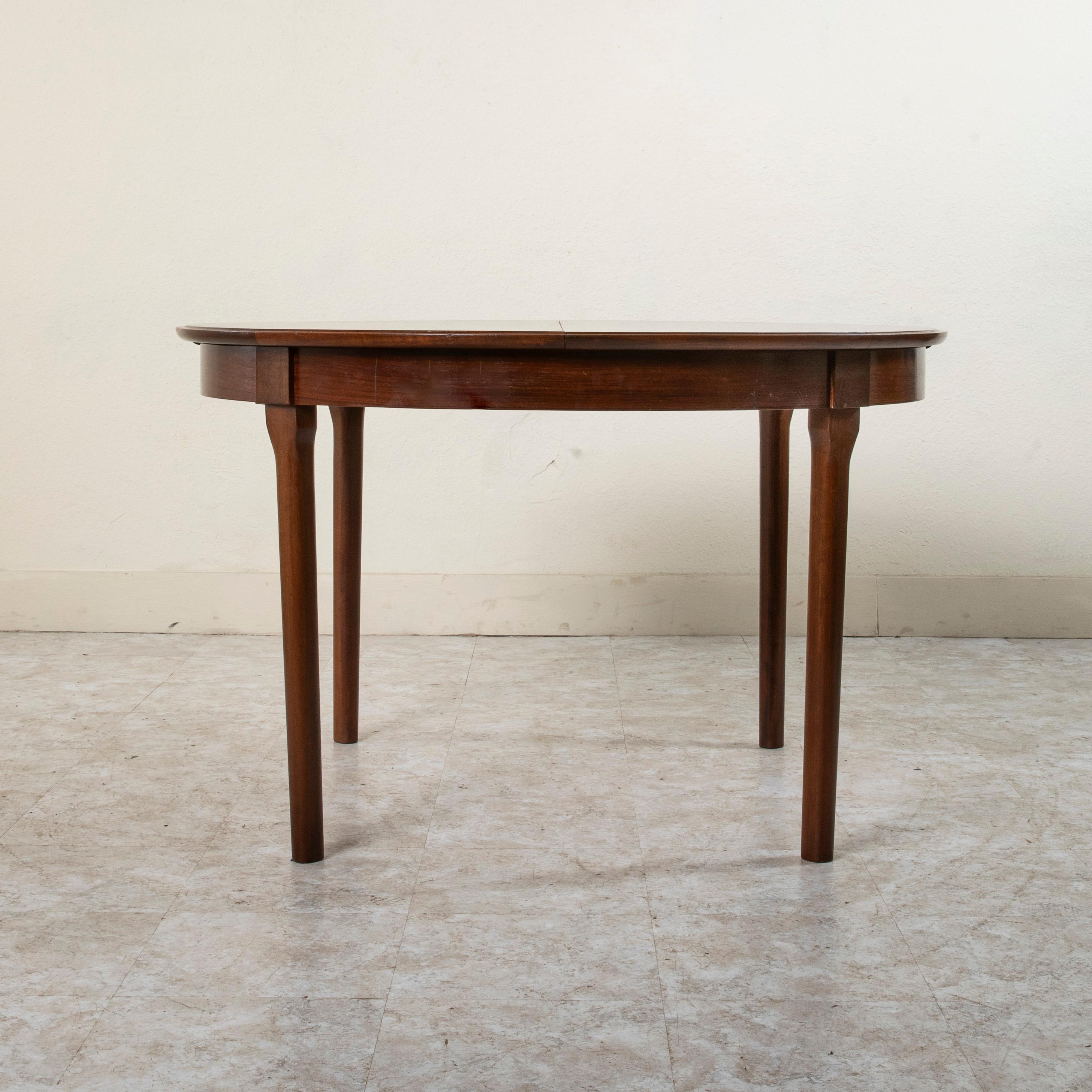 This Mid-Century Modern Danish dining table constructed of palisander or Brazilian rosewood features a 46.5 inch diameter top that rests on sleek tapered legs. The round top is divided in half and opens to allow access to its collapsible leaf. The