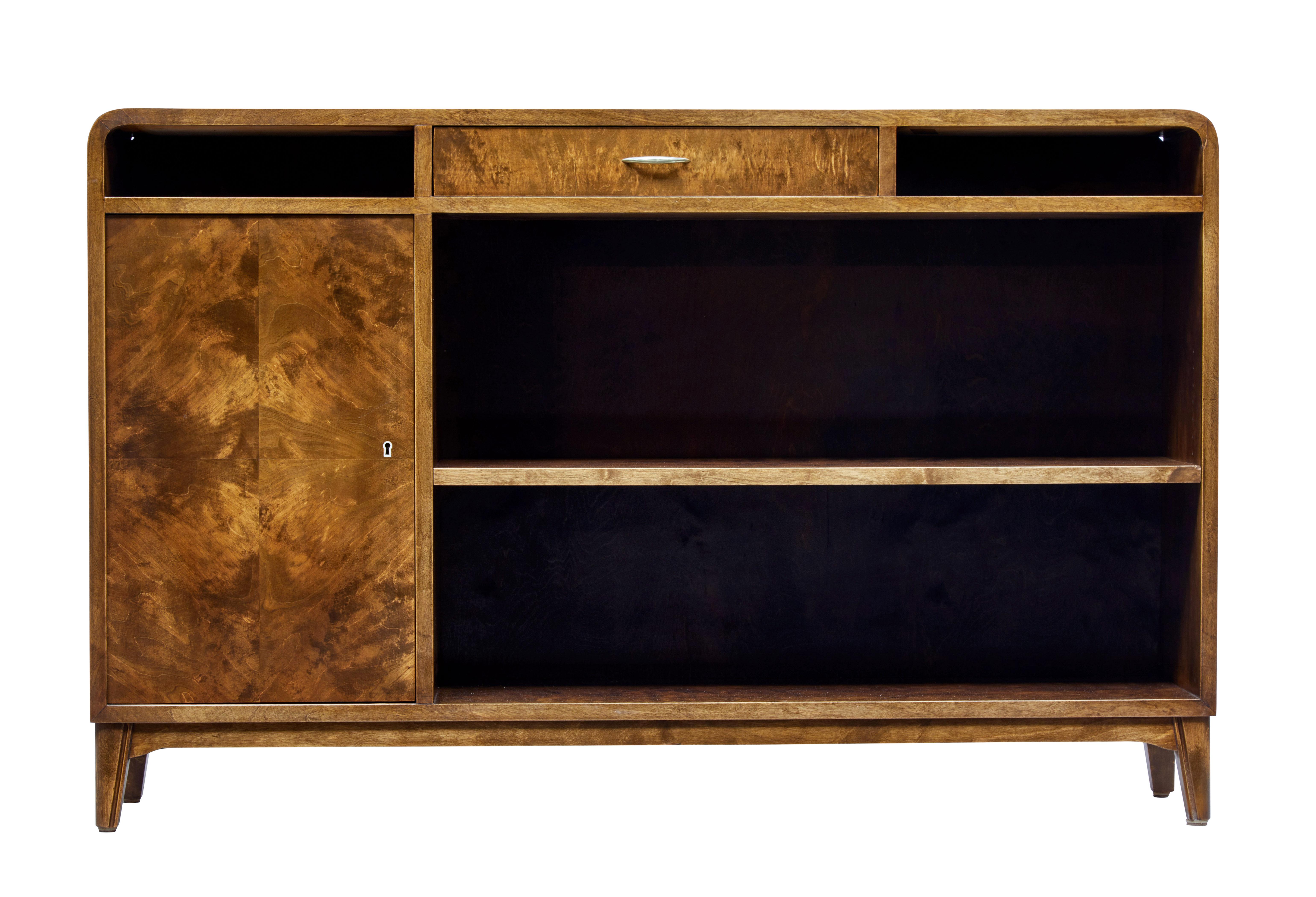 Scandinavian Modern dark stained bookcase, circa 1950.

Low bookcase with strong Art Deco influences. Rounded corners with central drawer, flanked either side by and open aperture. Single door cupboard to the left, with quarter veneer pattern to