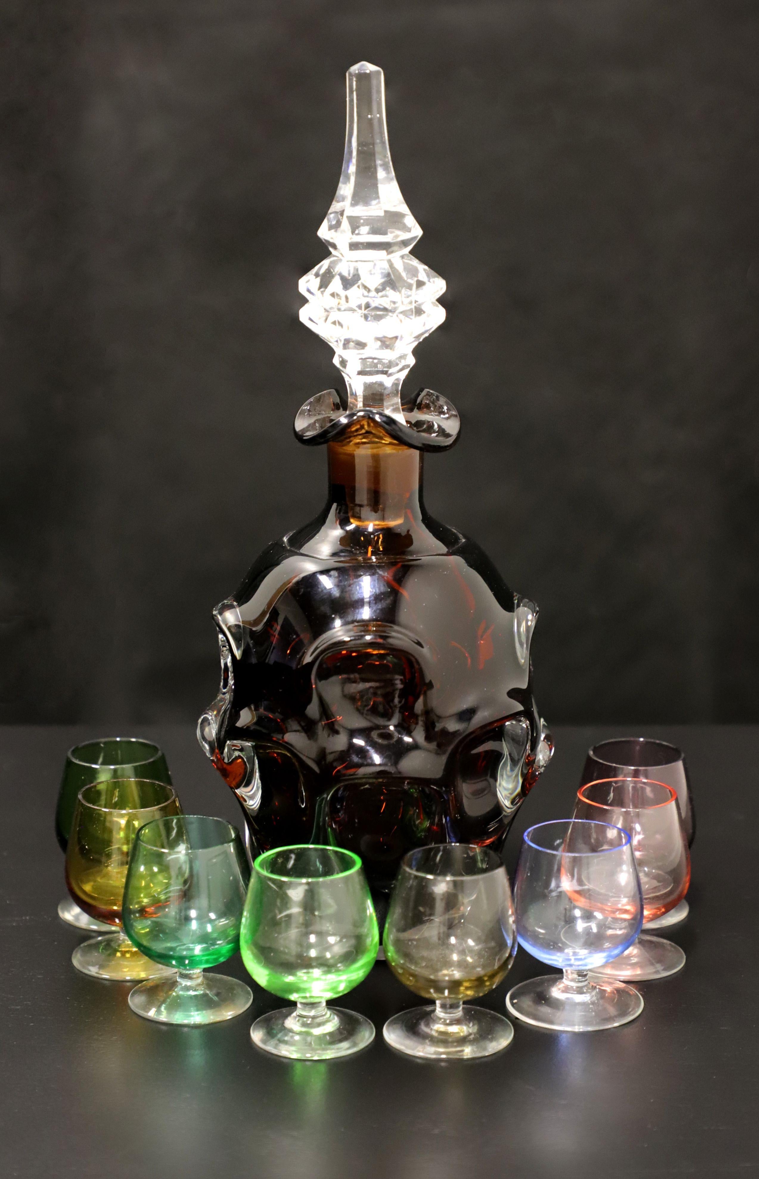 A Mid 20th Century amber glass decanter with stopper and eight various color cordial glasses. Amber glass decanter with blown circular bubble-like pattern and clear diamond-like cut finial shaped stopper. Includes eight complimenting various color