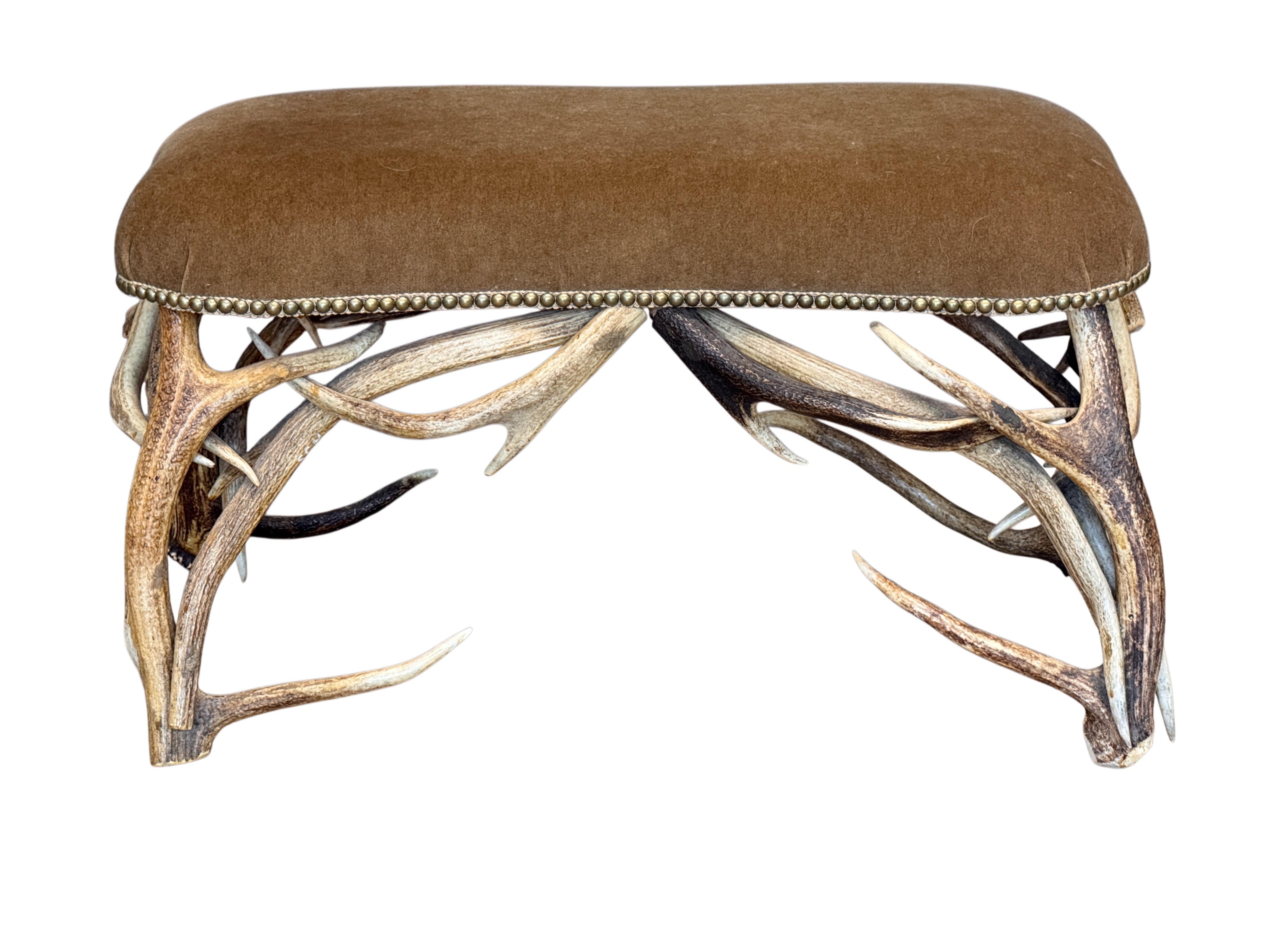 Mid-century ottoman constructed from naturally shed deer antlers, upholstered in rich wool mohair and finished with a border of brass nailhead trim. The sculptural antler base adds a rustic yet refined presence, blending natural materials with